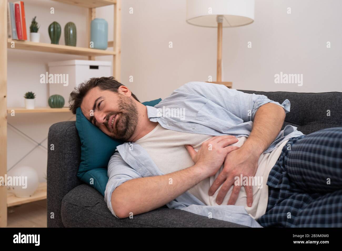El hombre tumbado en el sofá y la sensación de dolor de estómago Foto de stock