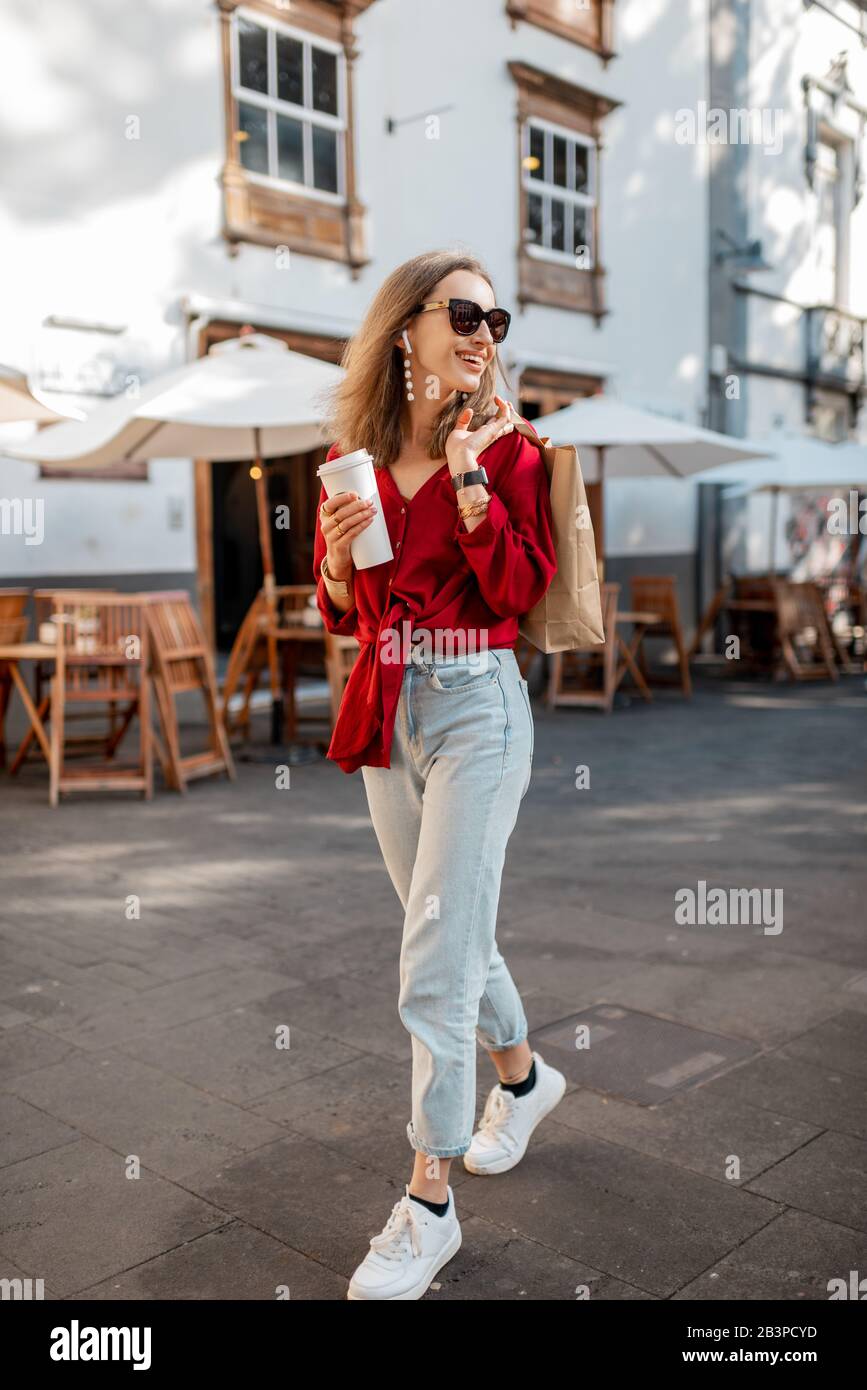 Estilo de vida retrato completo de una joven mujer con estilo vestido con  camisa roja caminando con taza de café en el casco antiguo en un día  soleado. Concepto de café para
