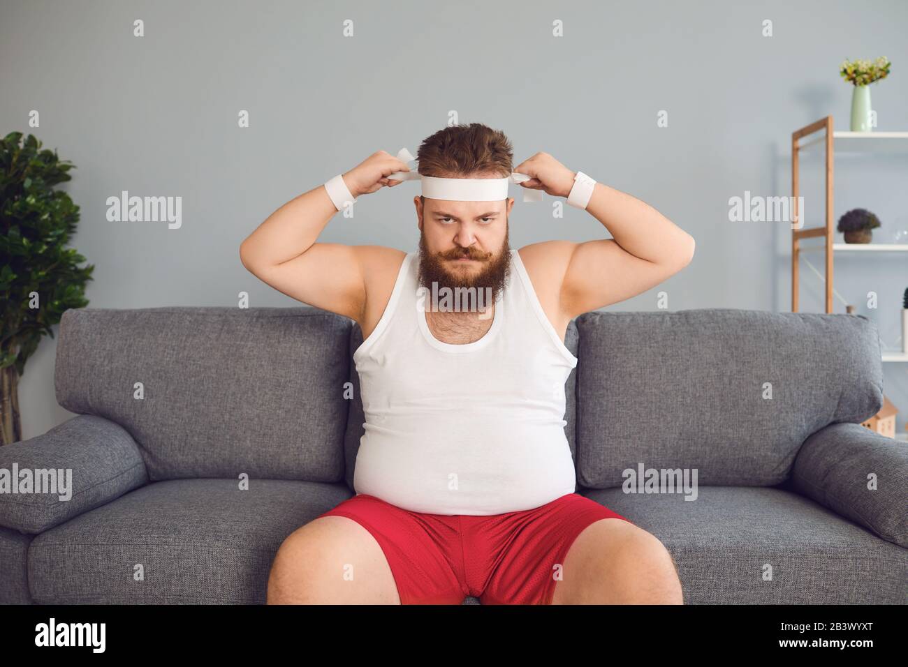El hombre gordo divertido en sportswear está sentado en el sofá en la  habitación Fotografía de stock - Alamy