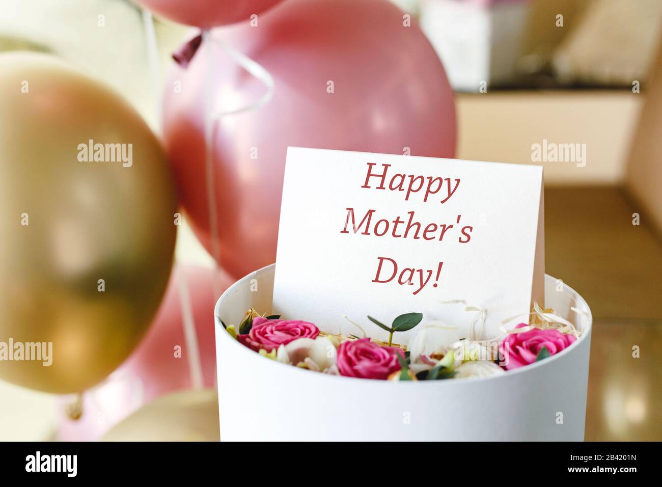 Texto del día feliz de la madre en la tarjeta de regalo en la caja de  flores cerca de globos de rosa y oro festivos. Tarjeta de felicitación para  mamá. Entrega floral,