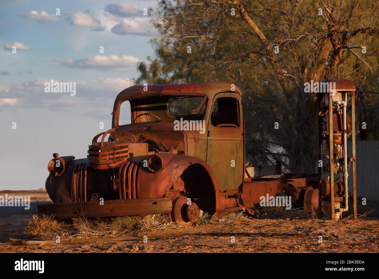 el viejo y oxidado naufragio abandonado del camión de recogida se encuentra abandonado en el lado de una carretera al atardecer Foto de stock