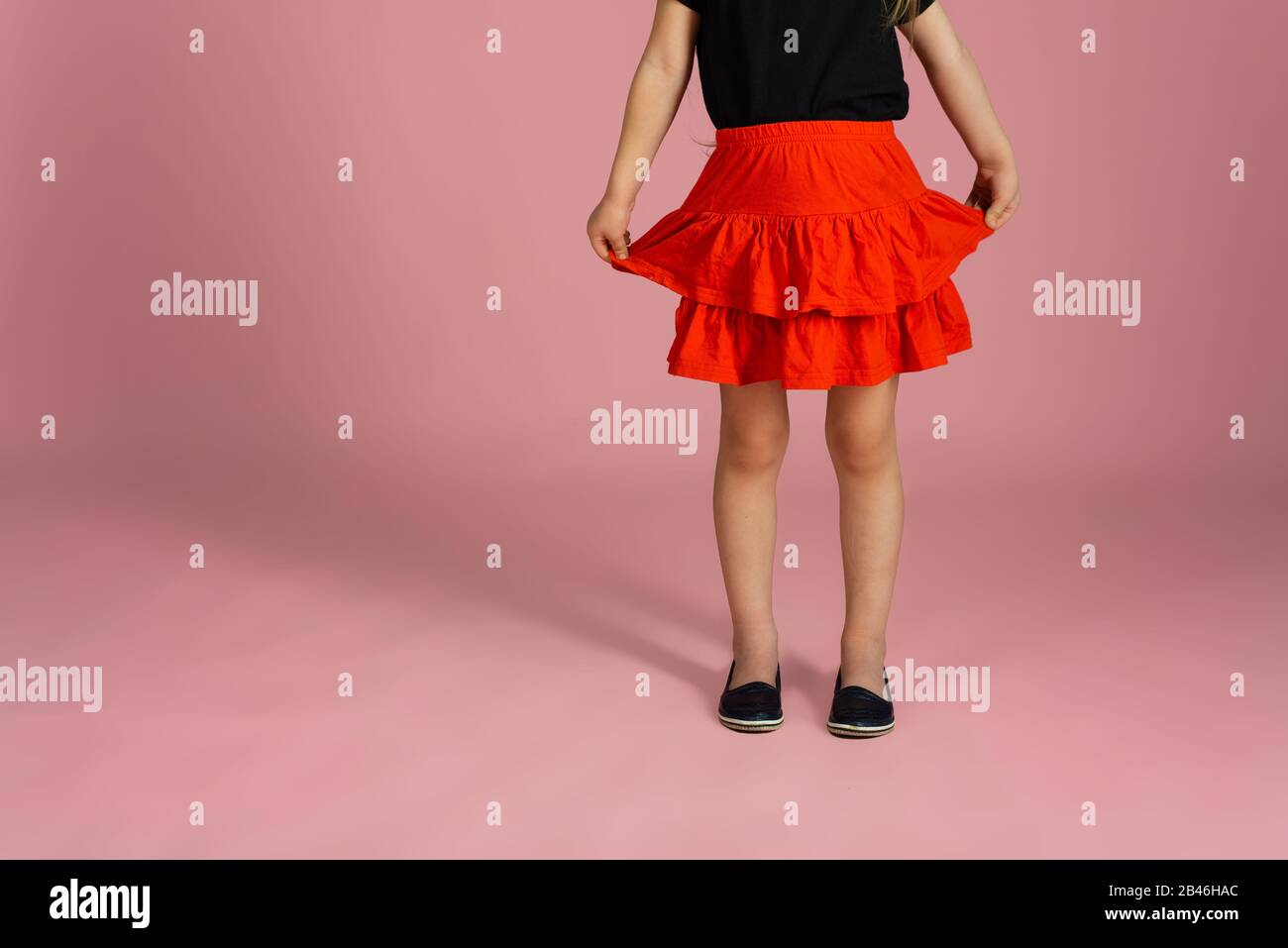 Las piernas de una niña en una falda roja y zapatos de ballet negro sobre  un fondo rosa. Primer plano. El concepto de niños, zapatos y ropa para  niños Fotografía de stock -