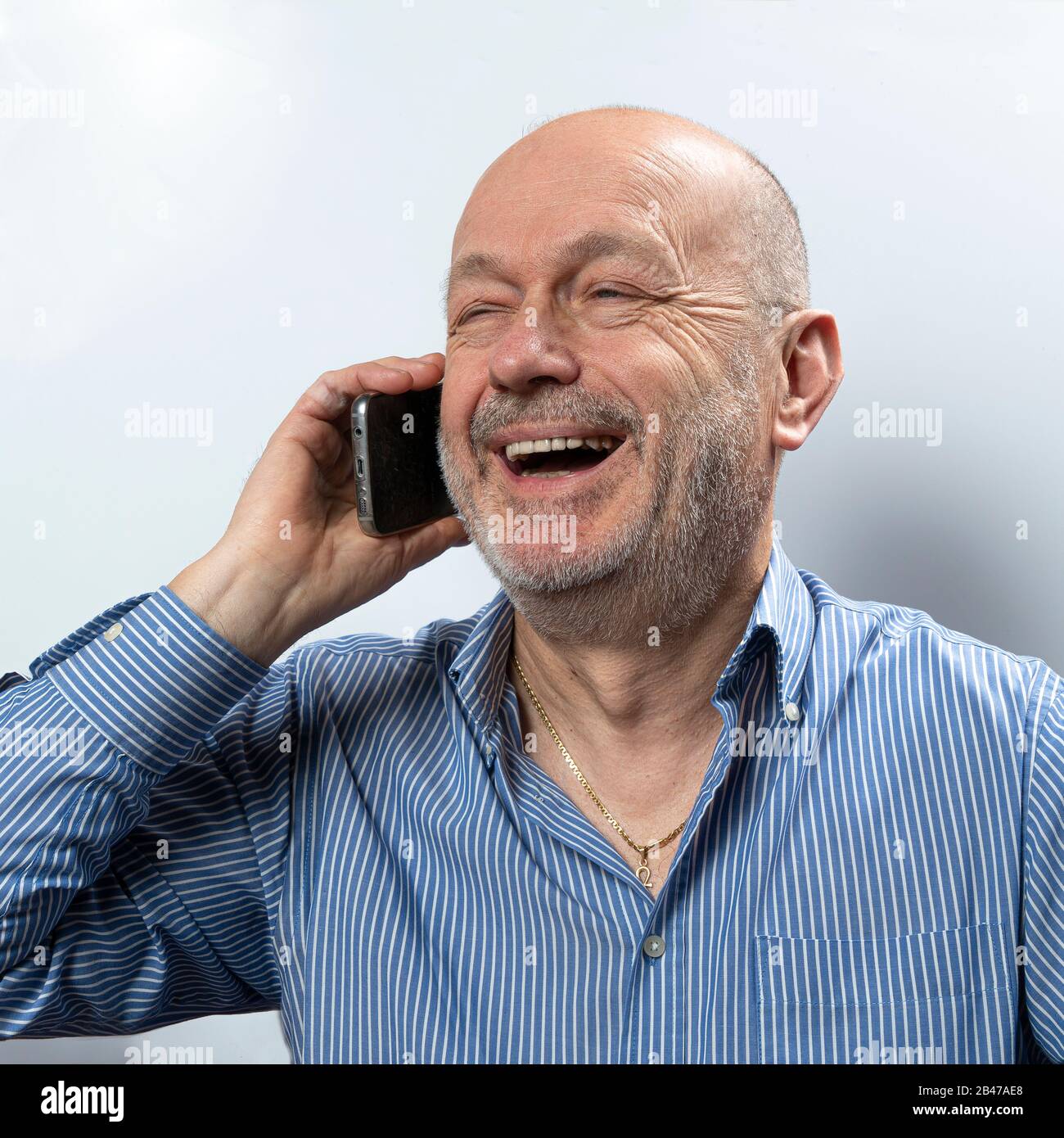 Un hombre de mediana edad se ríe durante una conversación con un teléfono móvil Foto de stock