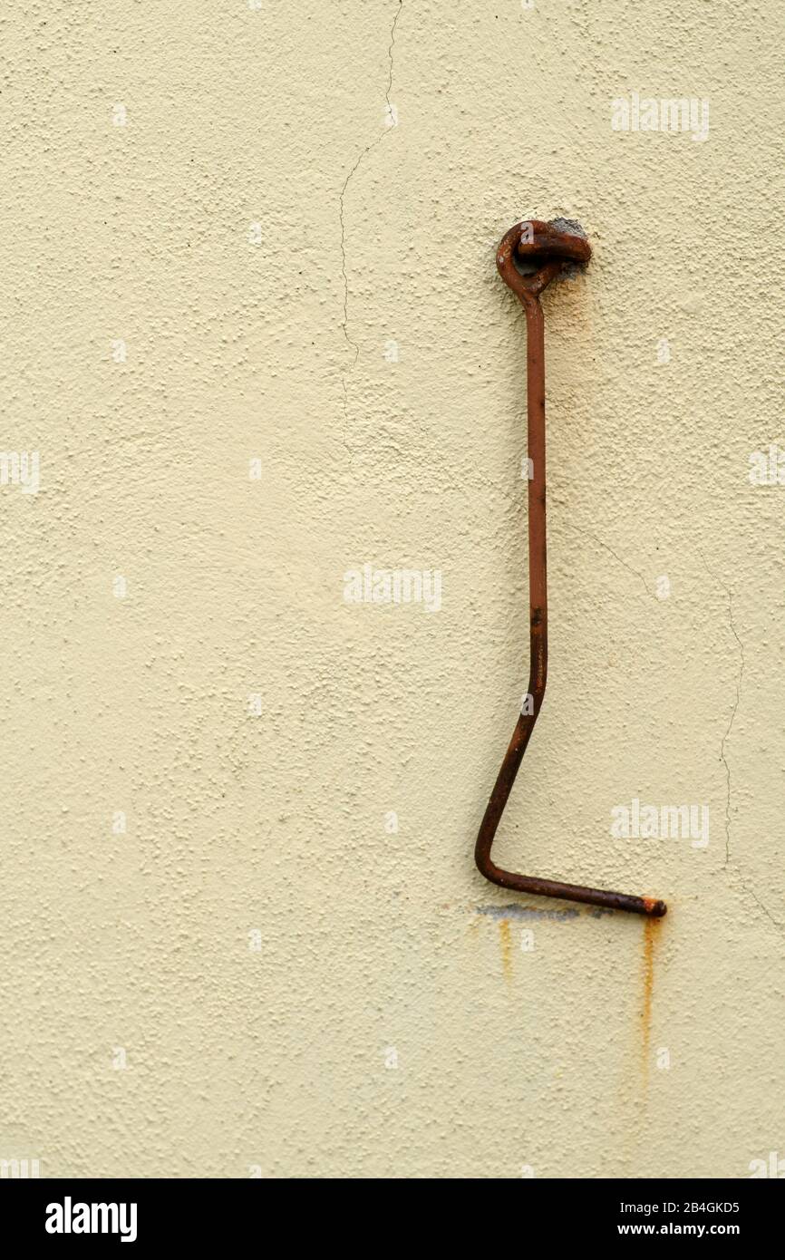 La vista de cerca de un gancho oxidado de la puerta en una pared de hormigón enyesado. Foto de stock