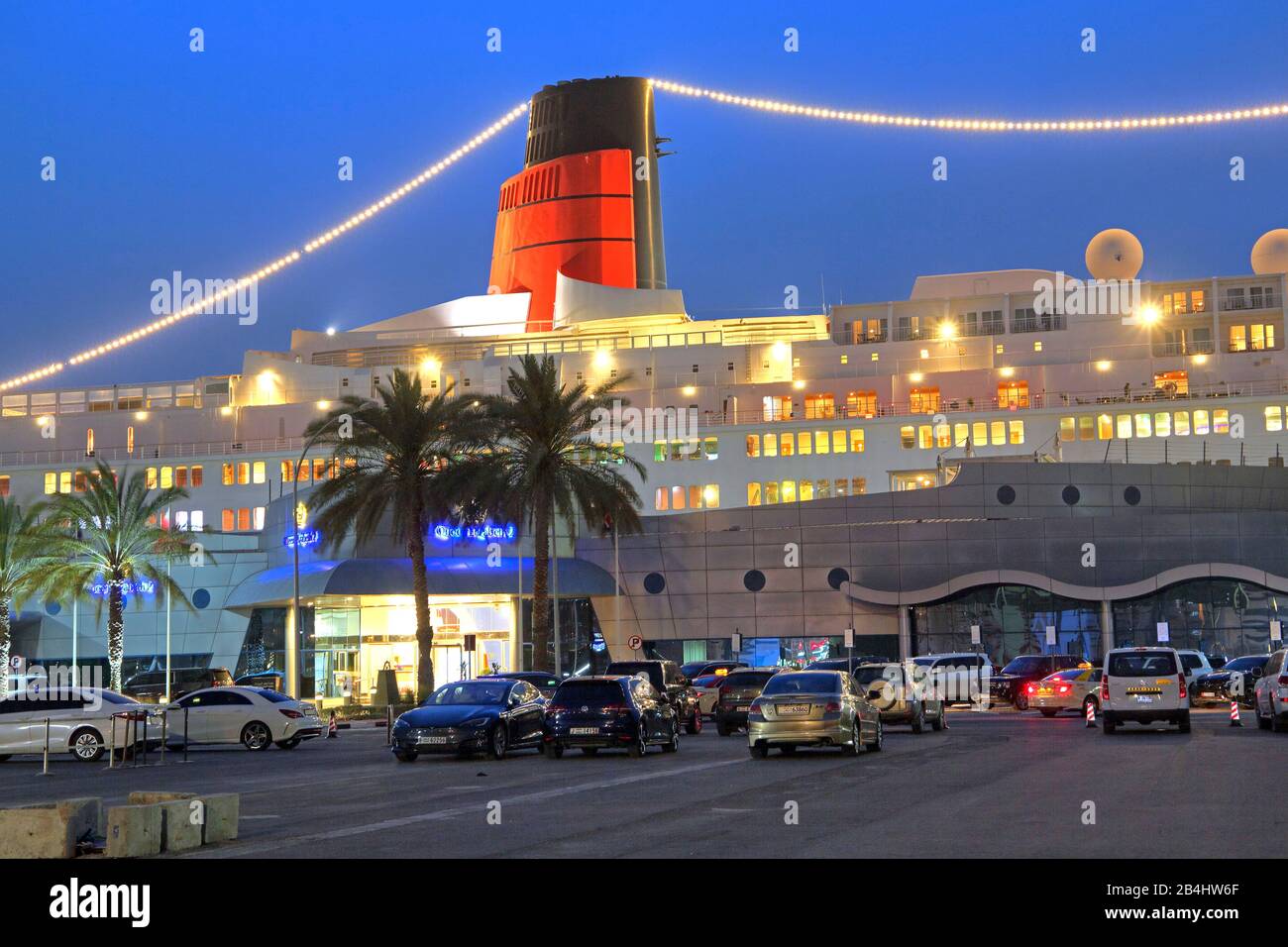 Hotel iluminado y barco museo Reina Isabel 2 (QE2) en el muelle al atardecer, Dubai, Golfo Pérsico, Emiratos Árabes Unidos Foto de stock