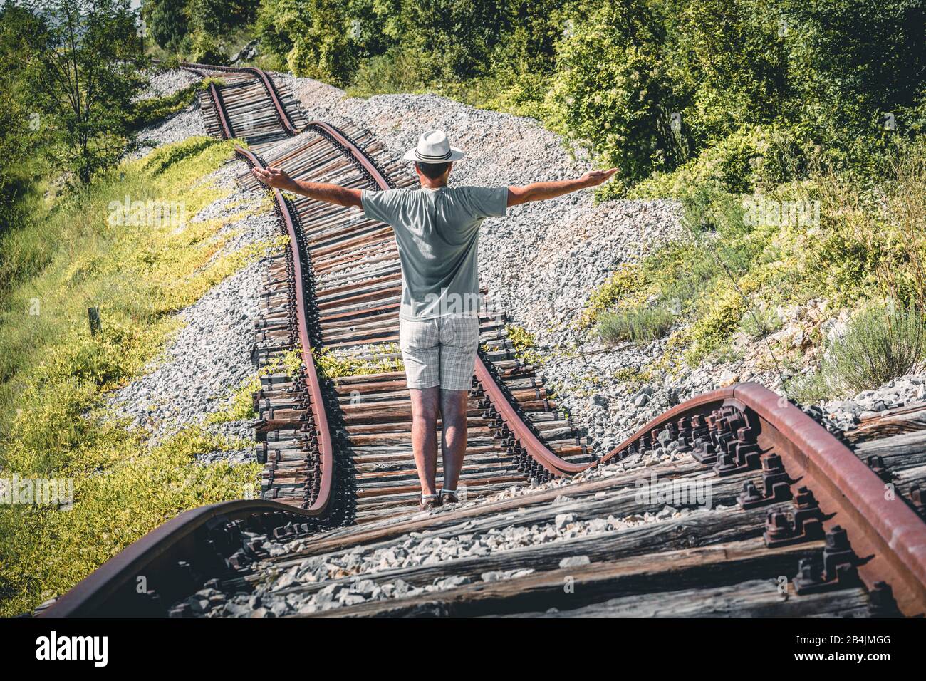 Un hombre con un sombrero blanco en medio de rieles abandonados parece querer detener un tren imaginario, Pijana pruga, Kozljak, Krsan, Istria County, Croacia Foto de stock