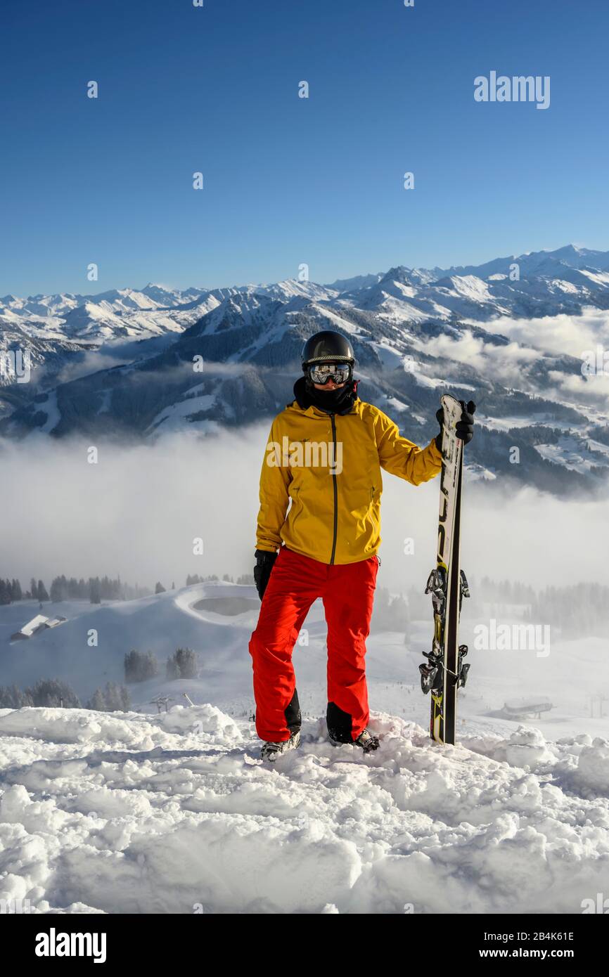 Esquiador parado en la pista de esquí sosteniendo el esquí, mirando hacia la cámara, paisaje nevado de la montaña, cumbre Hohe Salve, SkiWelt Wilder Kaiser Brixenthal Foto de stock