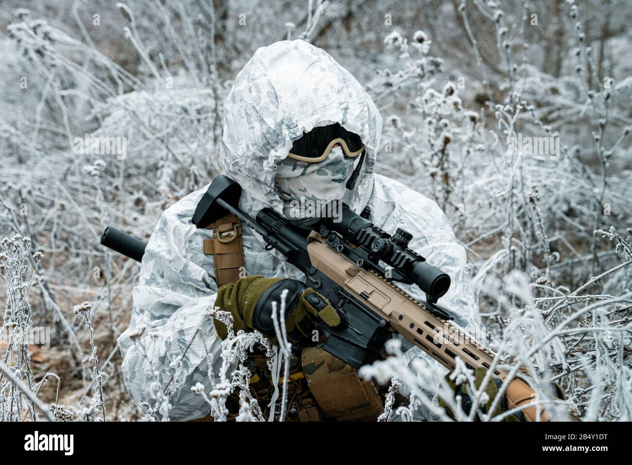 Hombre militar de primer plano con uniforme de camuflaje blanco con capucha  y machinegun en la larga hierba de invierno. Soldado se paró sobre el  arrodillado con machinegun Fotografía de stock -
