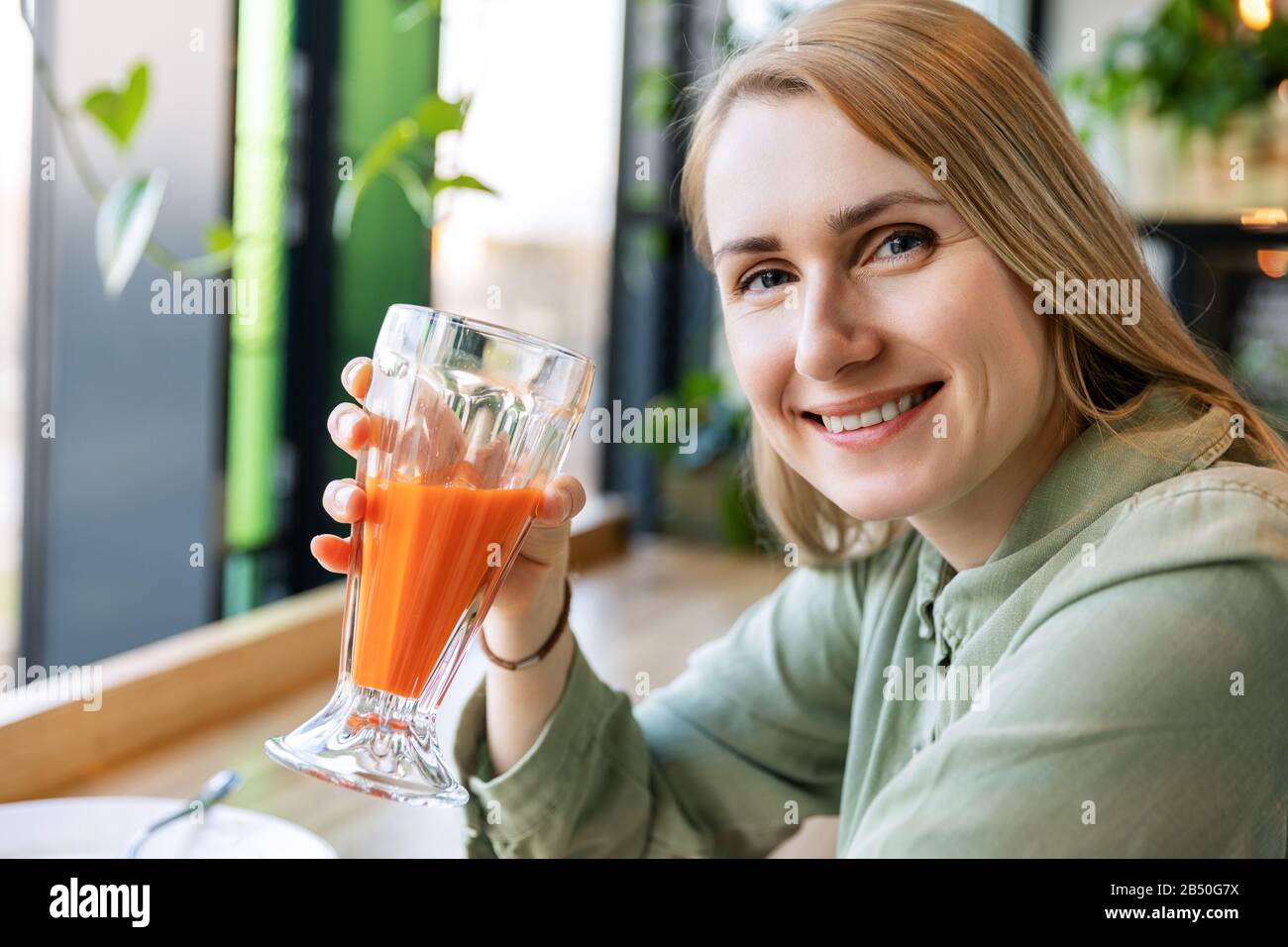 sonriente mujer de estilo de vida saludable bebiendo un vaso de jugo de zanahoria fresco Foto de stock