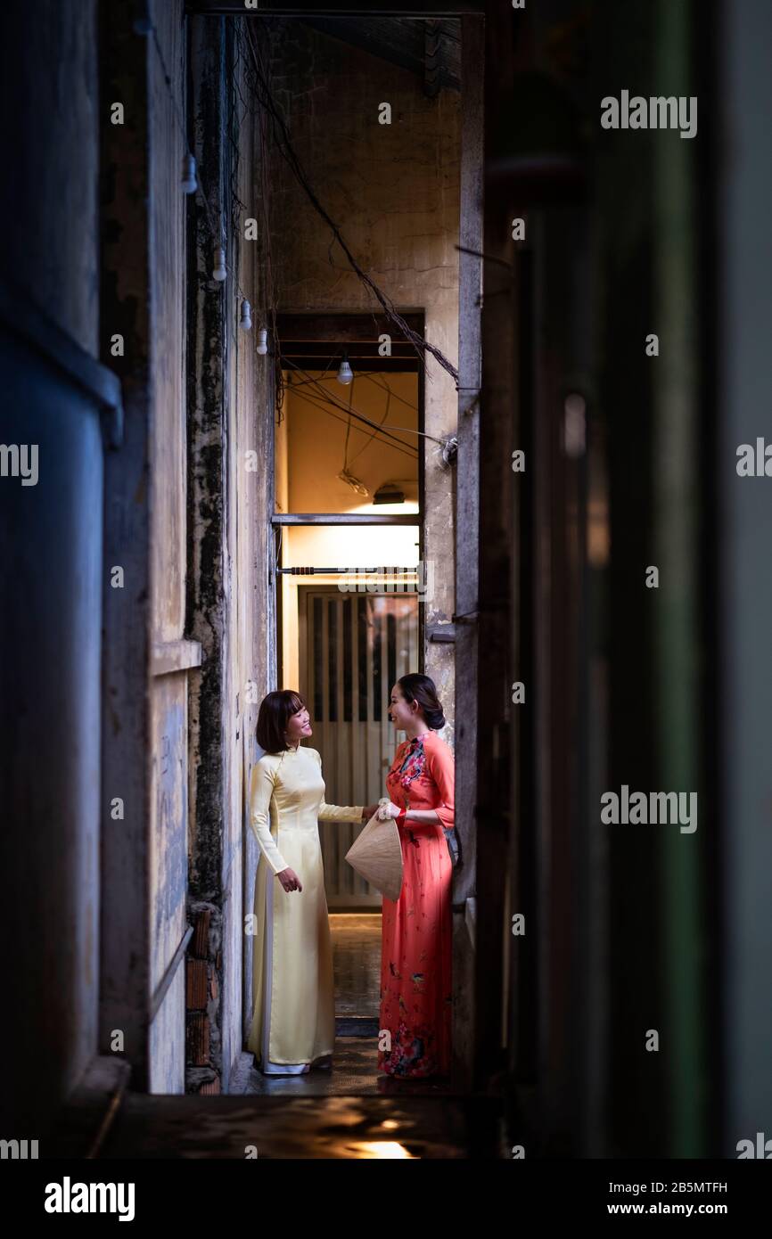 Dos mujeres jóvenes en Ao Dai se visten en un complejo de viviendas pobres en la antigua Saigón, Vietnam Foto de stock