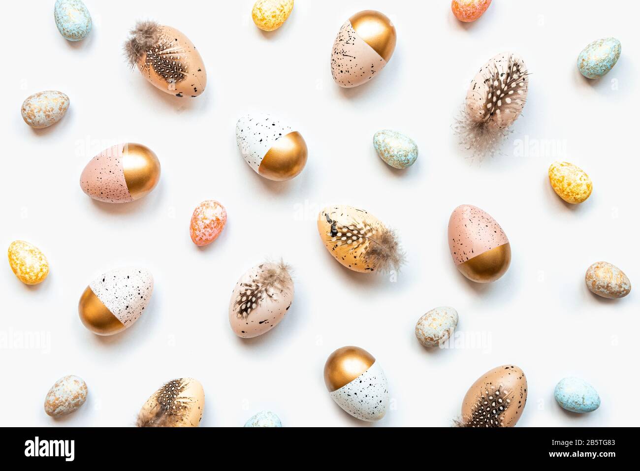 Vista superior de huevos de Pascua esparcidos coloreados con pintura dorada en diferentes patrones y colores. Fondo blanco. Foto de stock