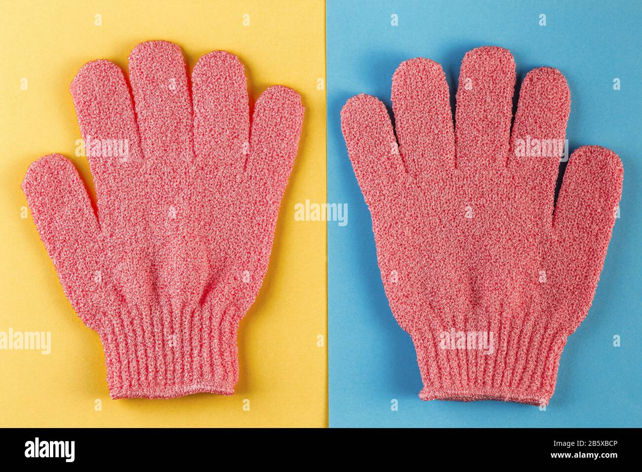 Un par de guantes de masaje de color rosa para ducharse sobre fondo azul y  amarillo. Guantes para usar en la ducha para masajes y exfoliación. Fondo  de belleza con cos Fotografía