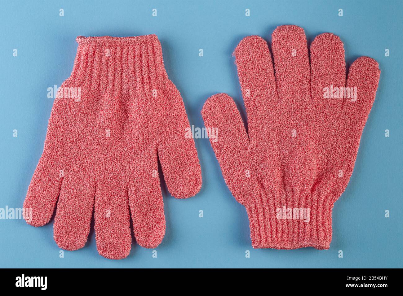 Un par de guantes de masaje rosa para ducharse sobre fondo azul. Guantes  para usar en la ducha para masajes y exfoliación. Fondo de belleza con  produ cosmético Fotografía de stock -