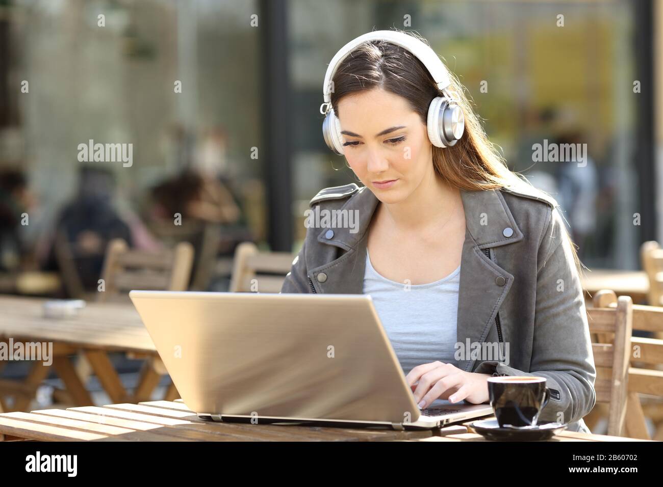 Una niña seria e-learning en su ordenador portátil con auriculares en una terraza de la cafetería Foto de stock