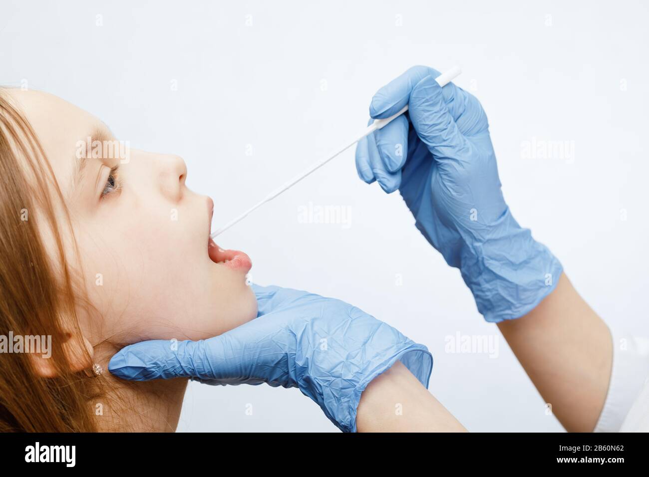 Pediatra o médico que toma la muestra de la prueba de saliva fom labios de la niña de edad elemental que realiza la prueba De Saliva (Salivaomics) procedimiento diagnóstico Foto de stock