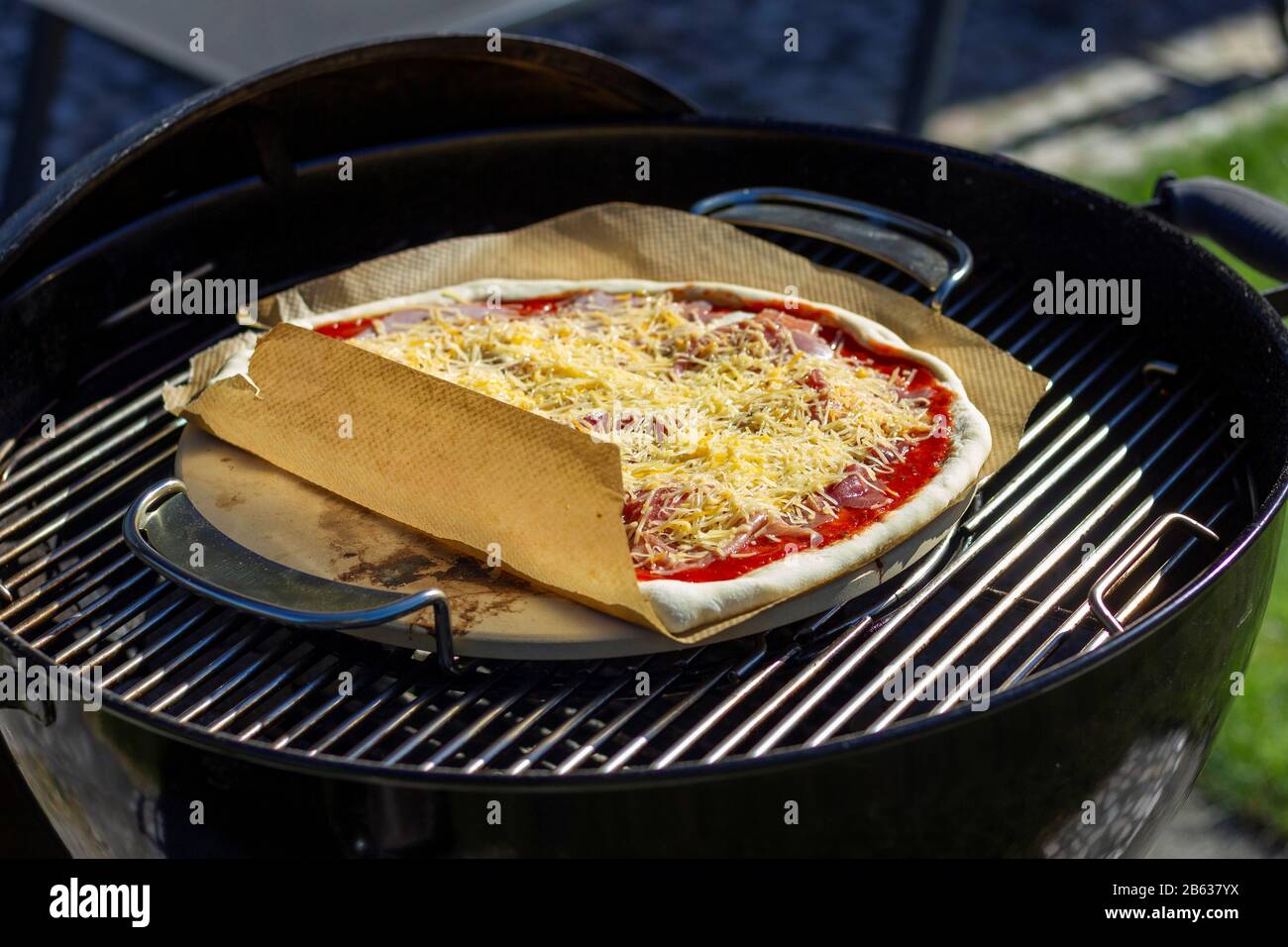 Un retrato de una pizza margherita acostada sobre una piedra de pizza y un  trozo de papel para hornear sobre una parrilla de carbón. La deliciosa pizza  tiene queso y t Fotografía