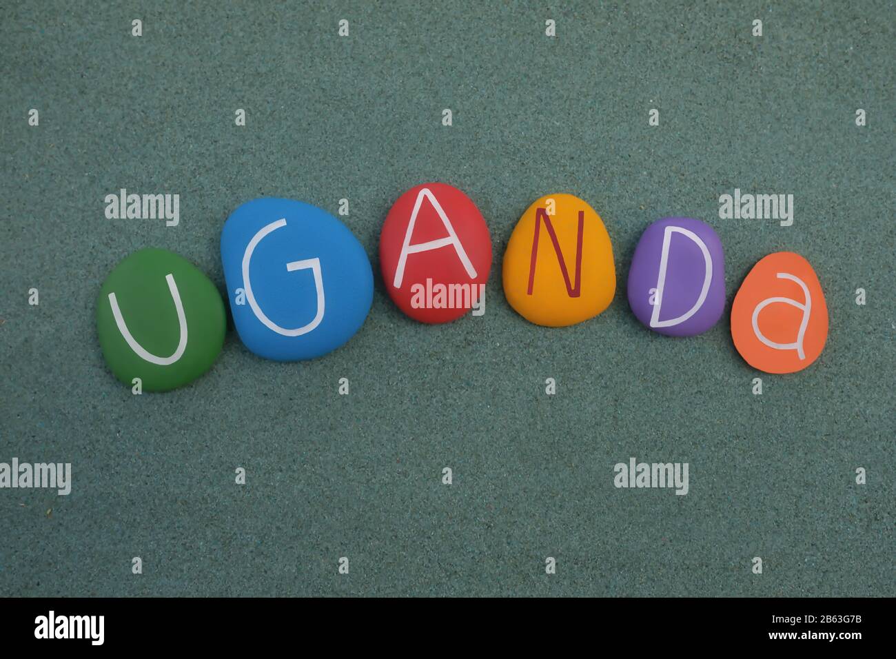Uganda país en el este-centro de África, recuerdo con letras de piedra multicolor sobre arena verde Foto de stock