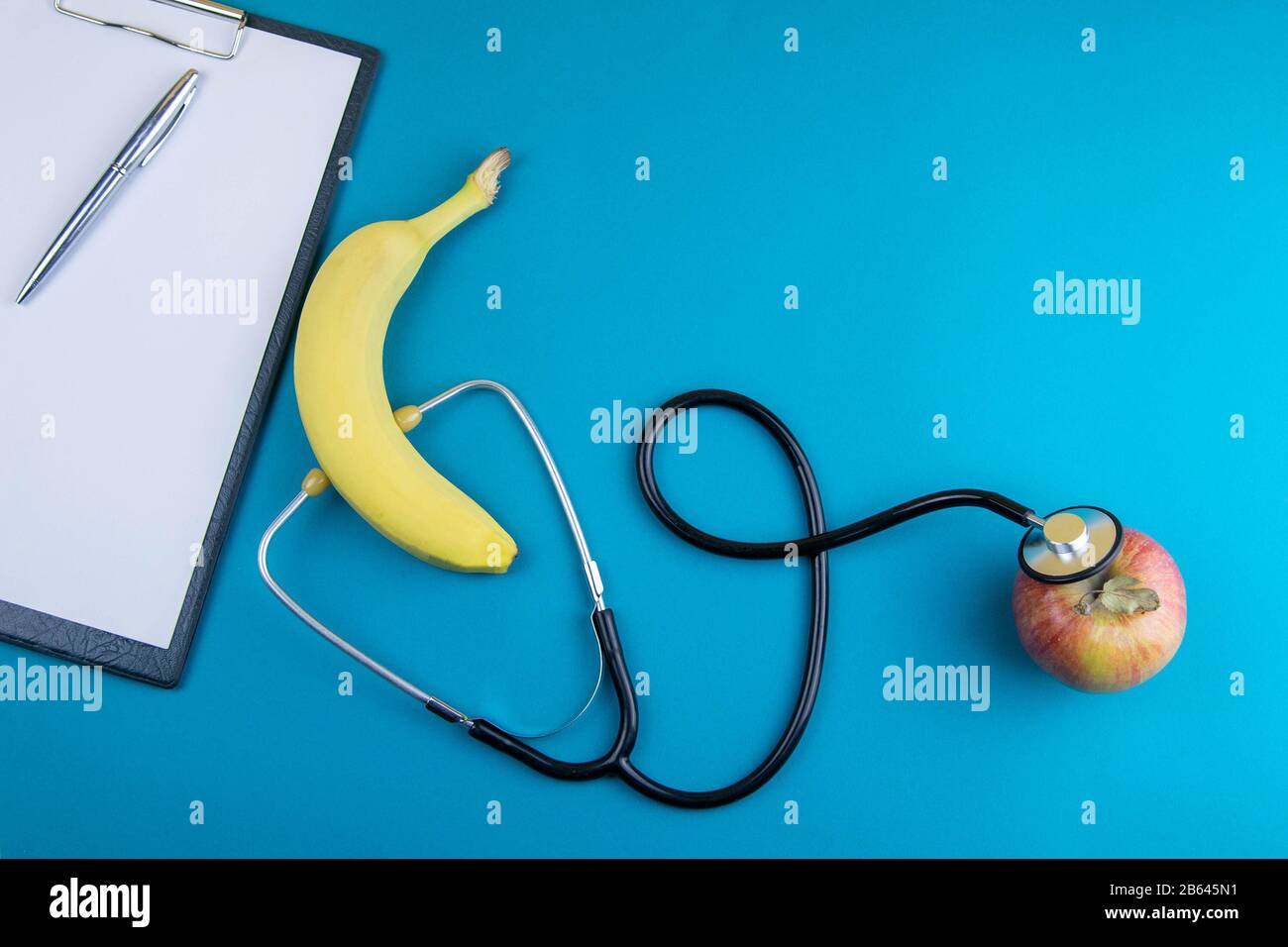 Un plátano está escuchando una manzana con un fonendoscopio, después está  una tableta con una hoja A4 y un bolígrafo Fotografía de stock - Alamy