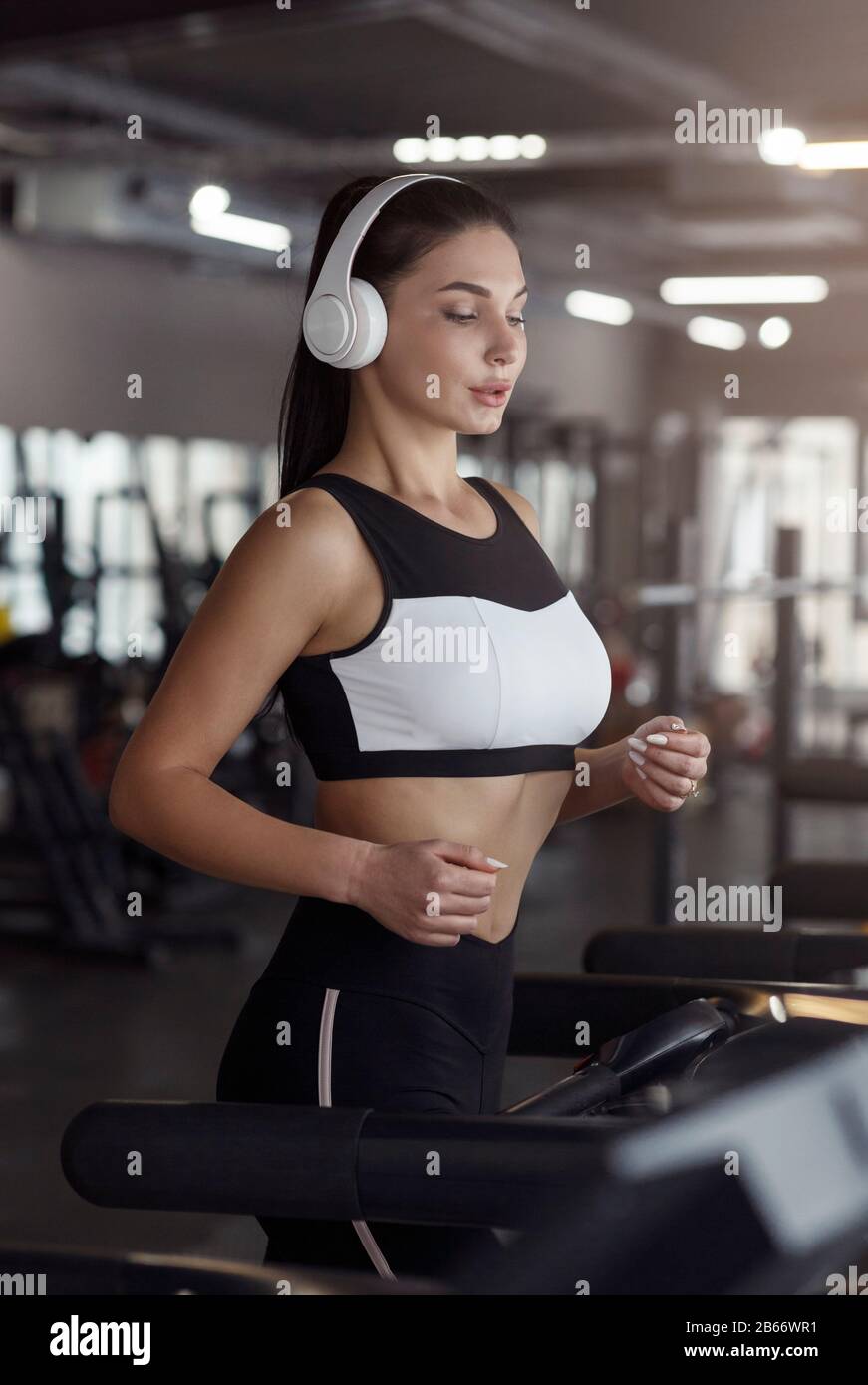 Ajuste a la mujer con auriculares y dispositivo móvil escuchando música en  la máquina de correr en el gimnasio Fotografía de stock - Alamy