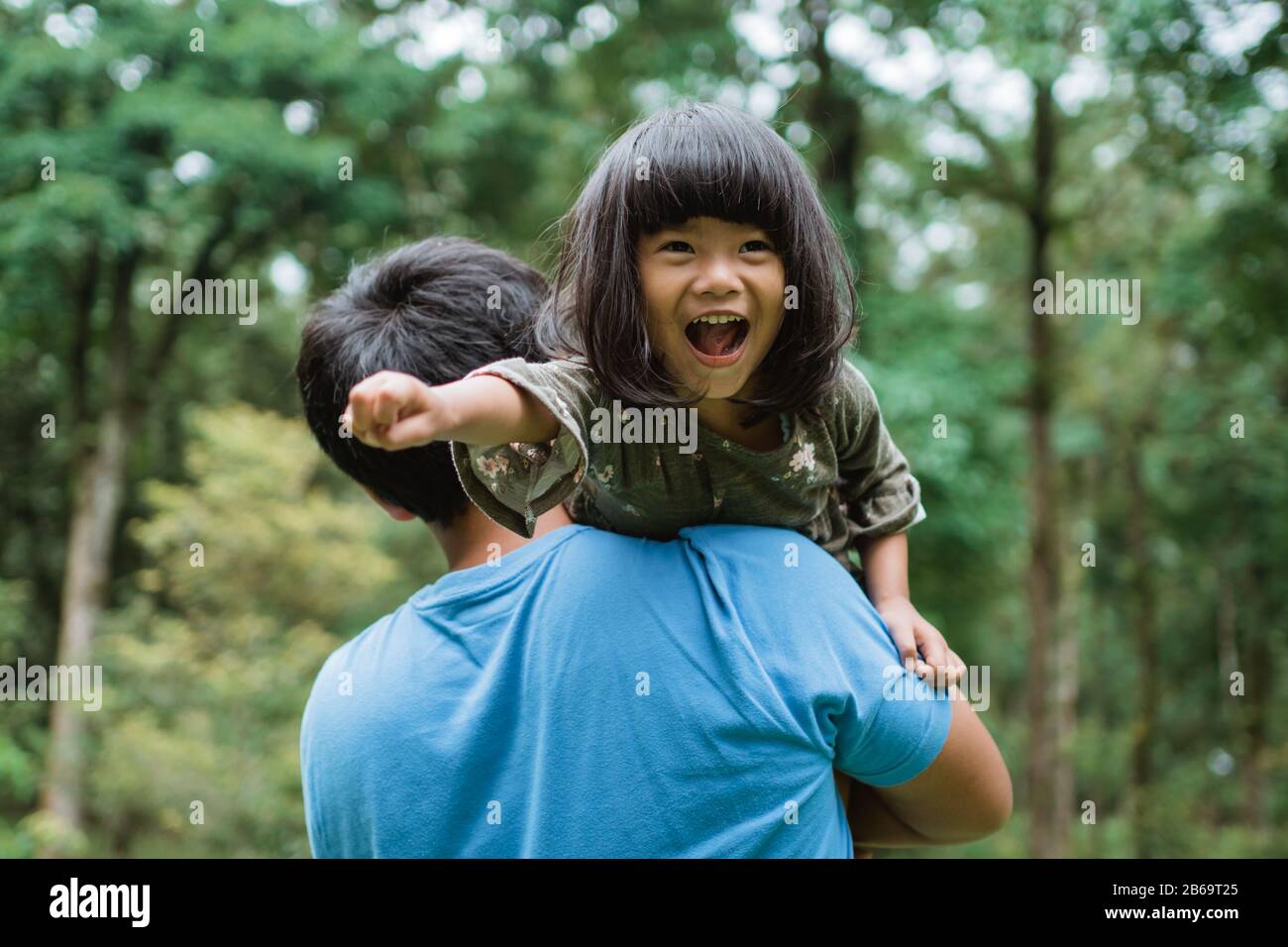 la niña se rió alegremente cuando fue llevada sobre el hombro de su padre mientras jugaba en el parque Foto de stock