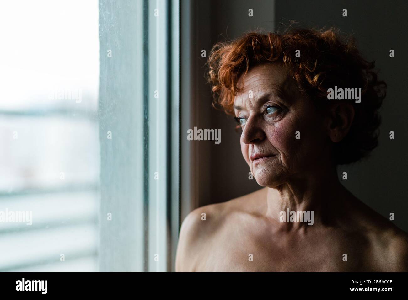 Mujer madura por la ventana pensando en la vida Foto de stock