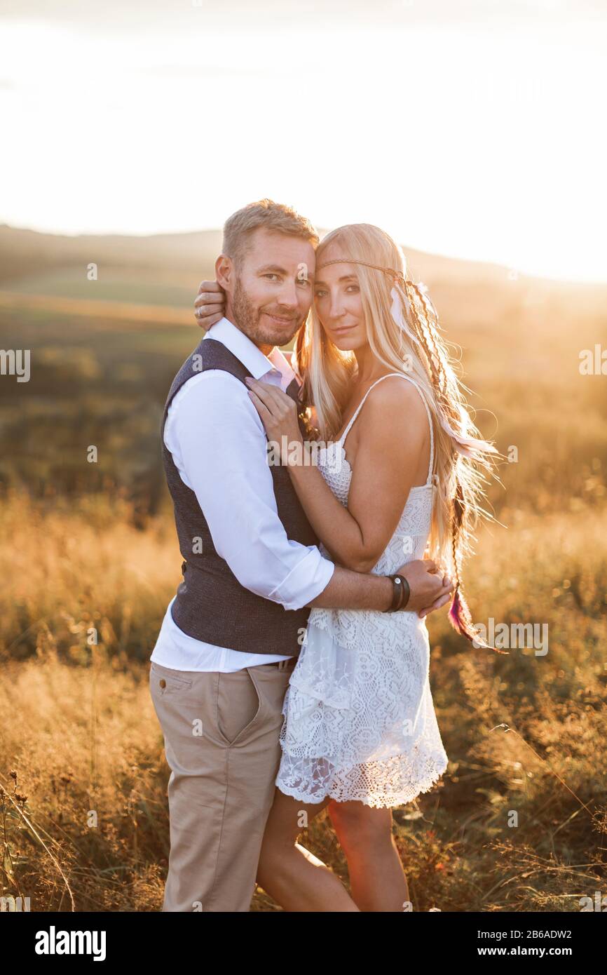 hermosa pareja vestida de estilo boho abrazándose a otros en el soleado campo de verano. Hombre guapo en ropa y mujer en vestido blanco y Fotografía de - Alamy