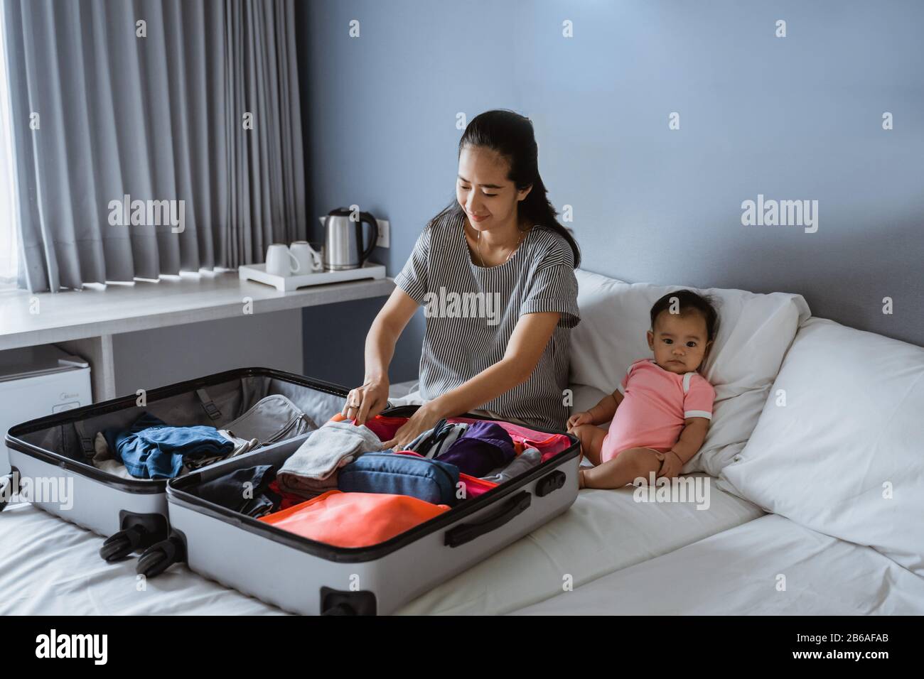 el bebé se sienta junto a la madre preparando la ropa para poner en la  maleta Fotografía de stock - Alamy