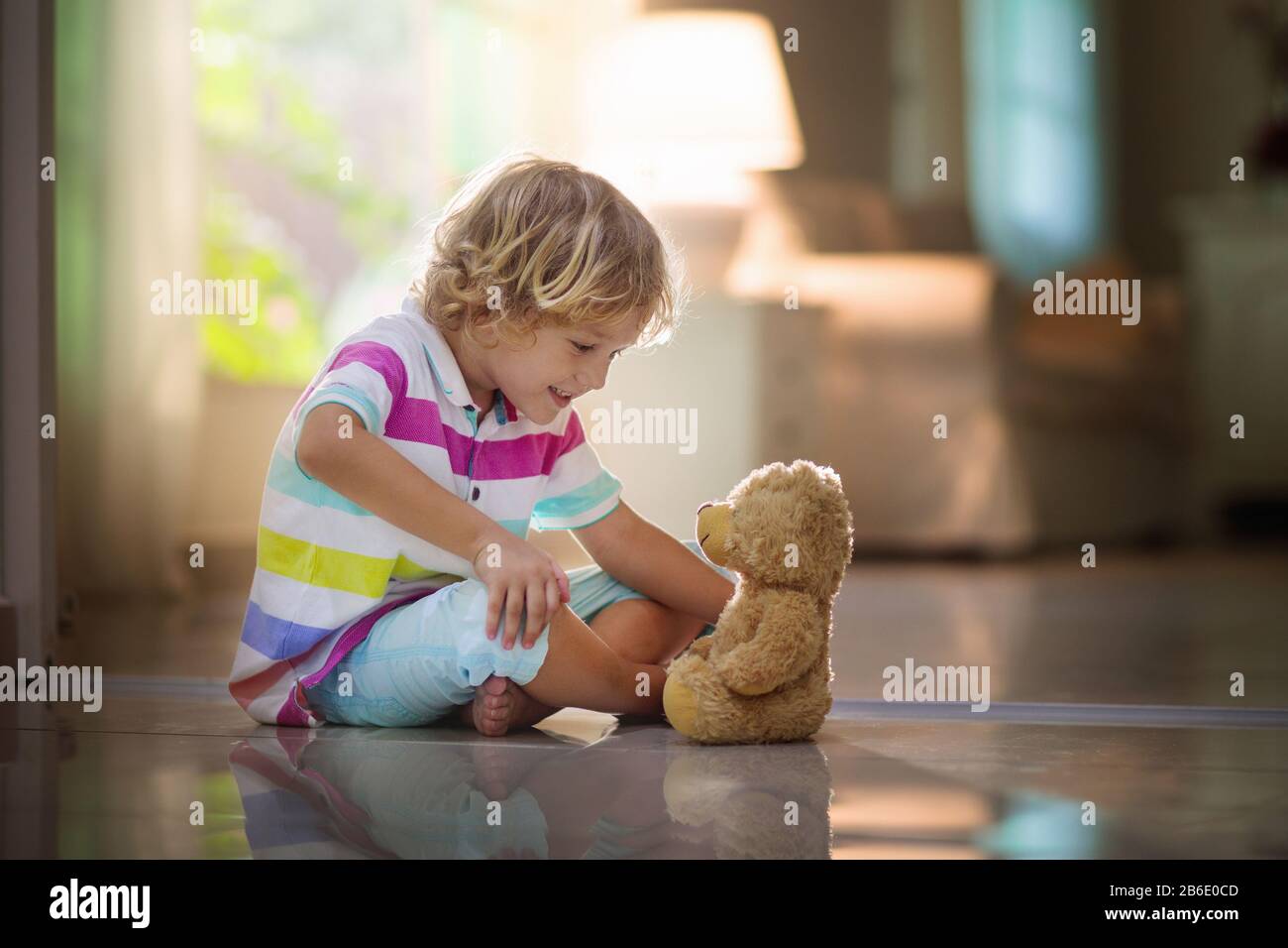 Niño jugando con oso de peluche. Niño pequeño que se jovía de su juguete favorito. Niño y peluche en casa. Niño sentado en el piso de la sala de estar con b