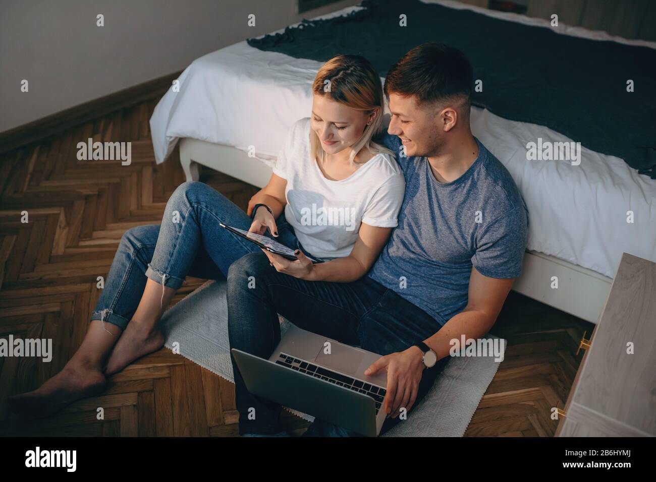 Vista superior de una pareja caucásica sentada en el suelo y usando aparatos modernos mientras sonríe y disfruta Foto de stock