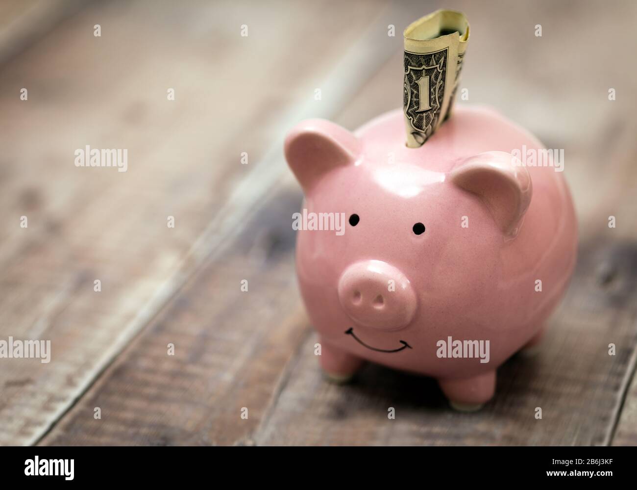 Un billete de un dólar insertado en un banco de piggybank rosa. Ahorro de dinero y bienestar financiero. Foto de stock