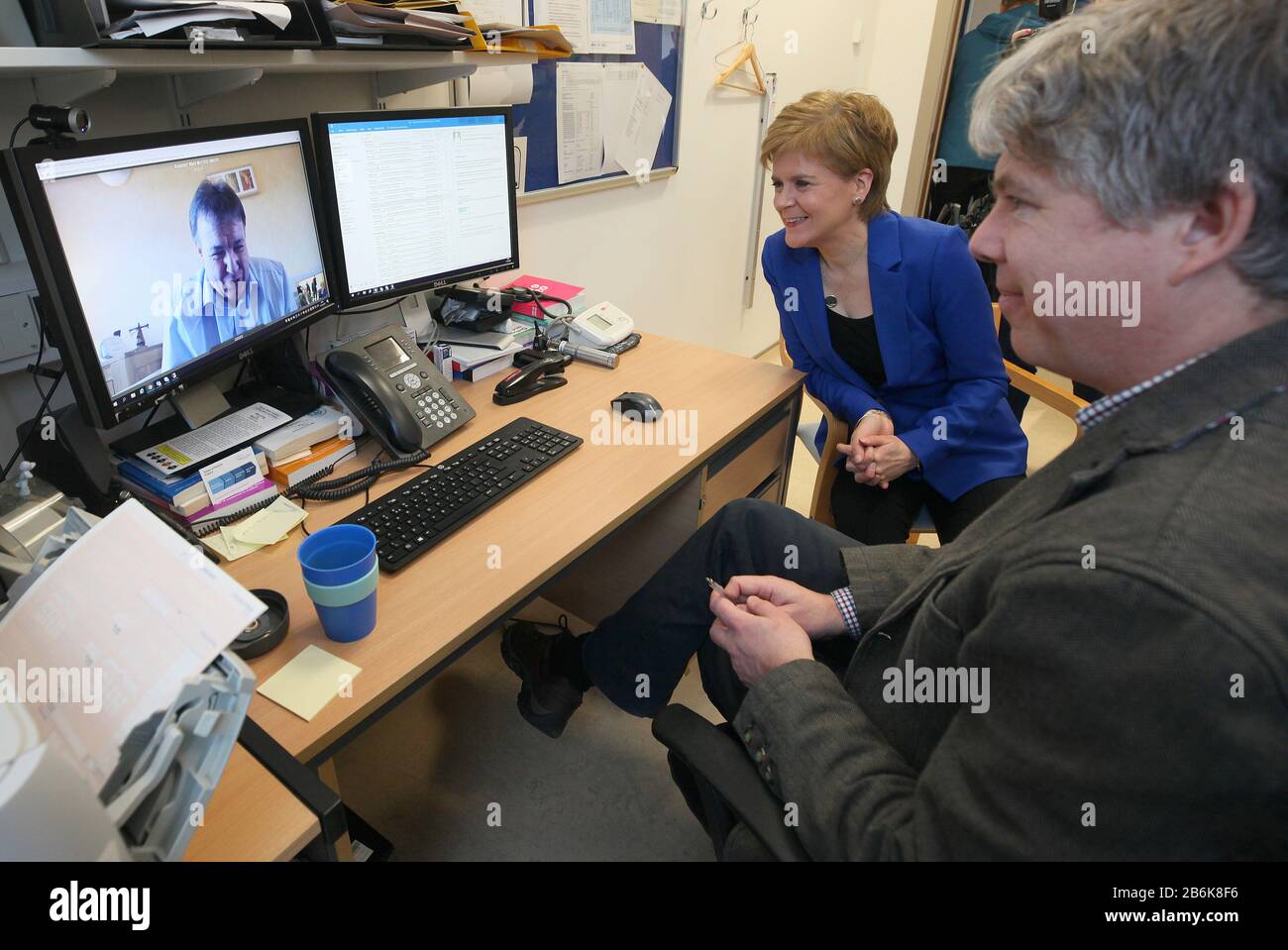Nicola Sturgeon, primer Ministro escocés, se sienta en el Dr. Peter Cairns realizando una consulta en video en el Centro de vida saludable Wester Hailes en Edimburgo, con un paciente de su propia casa. Foto de stock