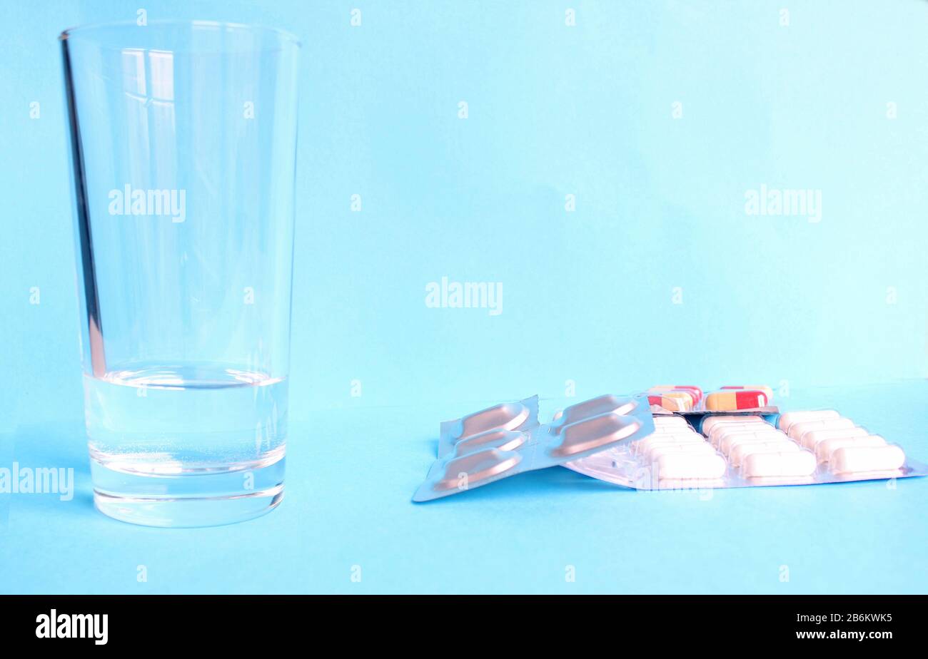 Vaso de agua y pastillas aisladas sobre fondo azul Foto de stock