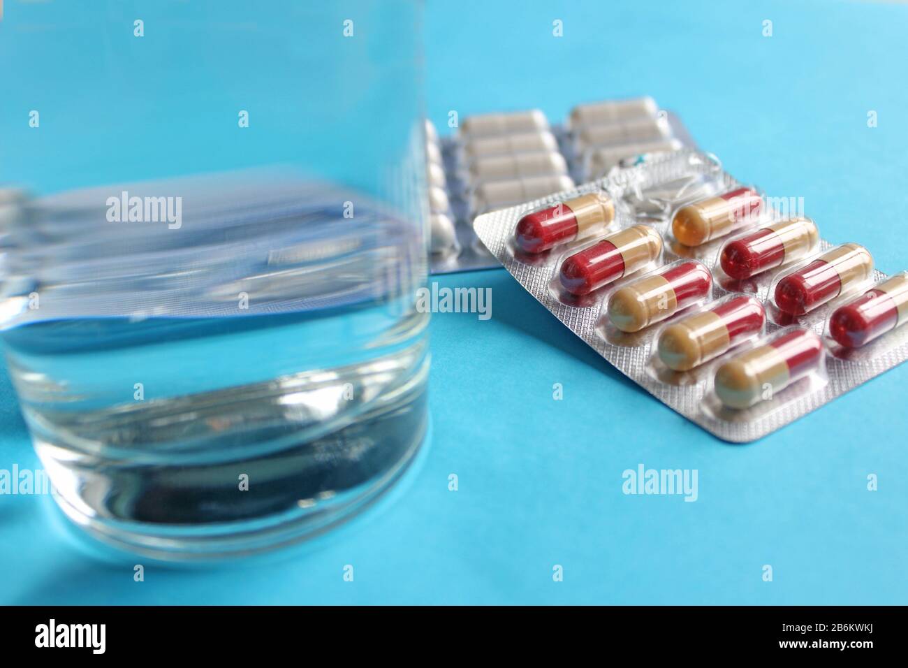 Pastillas blancas con cristal de agua clara sobre fondo azul, vista superior con espacio de copia. Concepto de farmacia médica Foto de stock