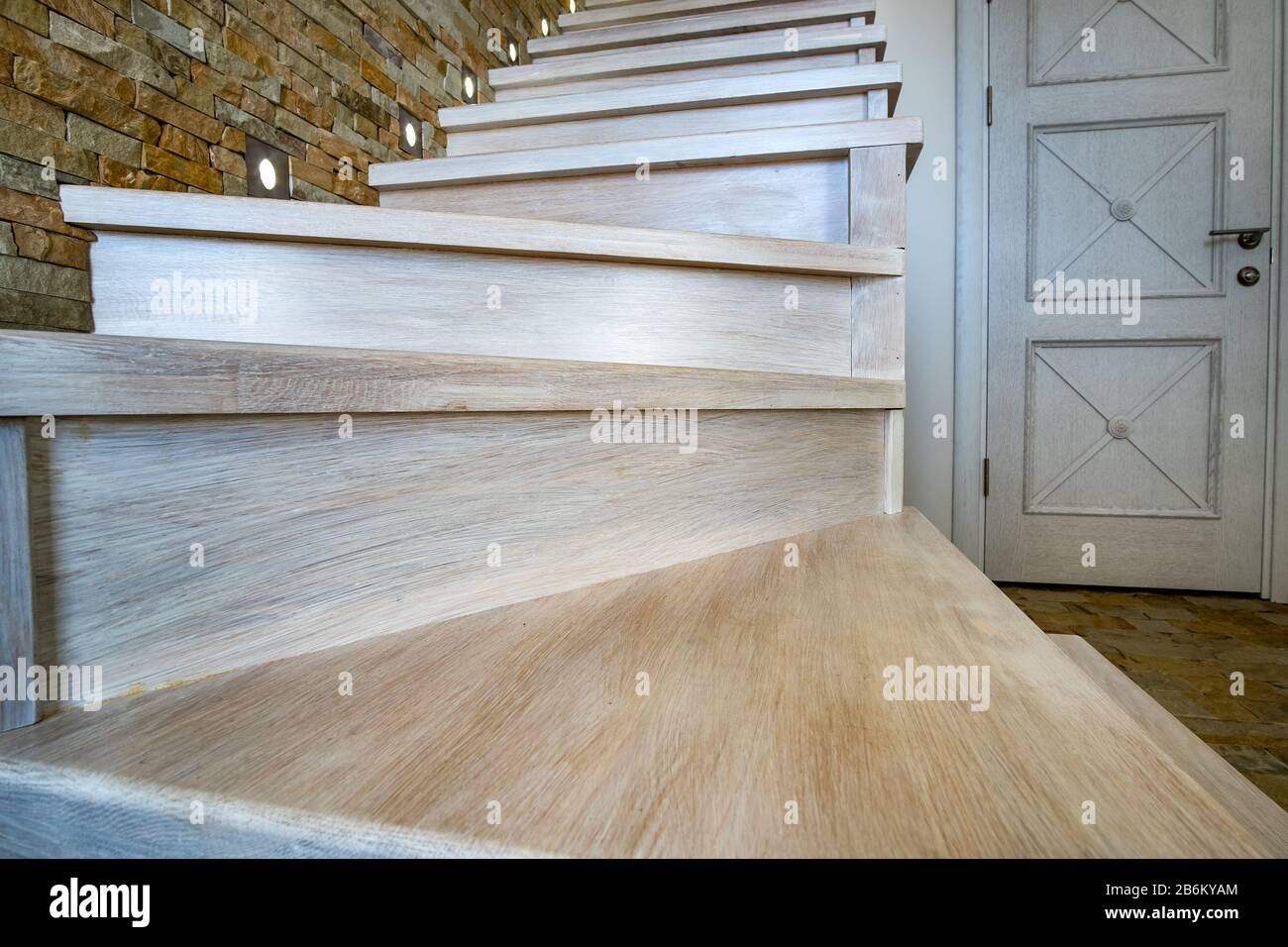 Elegante escalera contemporánea de madera en el interior de la casa loft. Pasillo moderno con paredes decorativas de ladrillo de piedra caliza y escaleras de roble blanco. Foto de stock