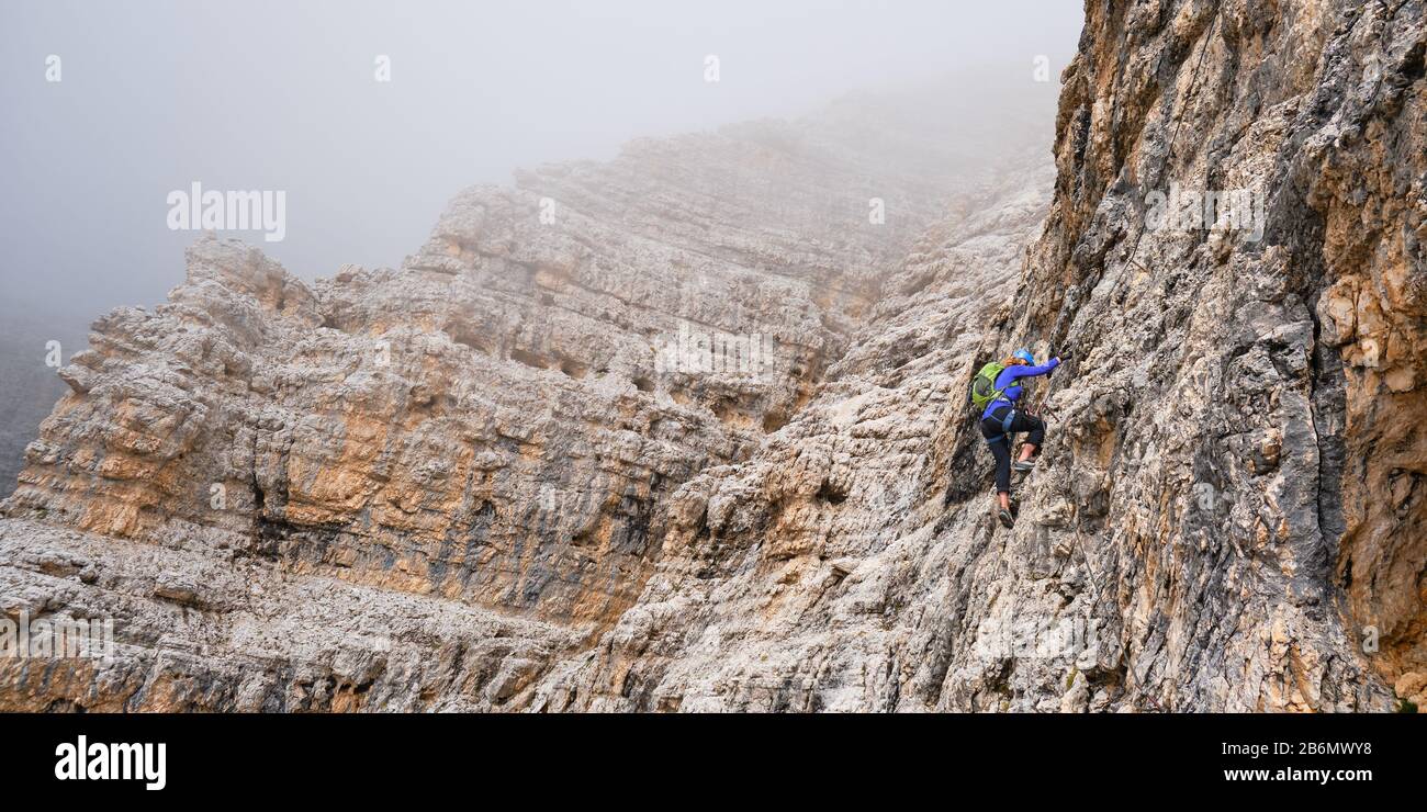 Mujer en vía ferrata Cesare Piazzetta, moviéndose hacia arriba a través de las nubes bajas. Vacaciones activas en Sella grupo, Dolomitas montañas, Italia. Foto de stock