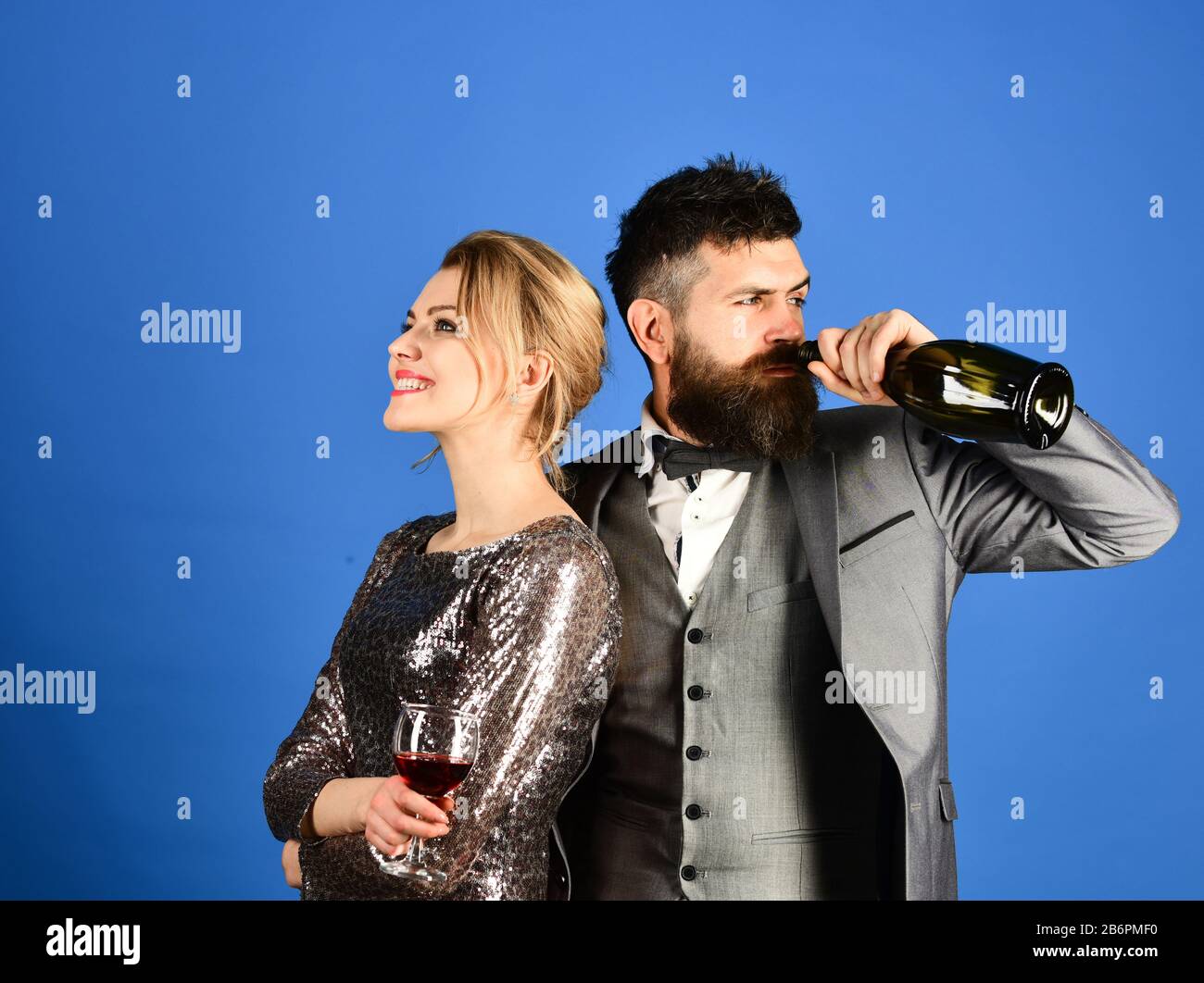 Dama y caballero sosteniendo una copa de vino y bebiendo de una botella.  Hombre con barba y mujer vestido sobre fondo azul. Pareja enamorada de la  degustación de vino italiano con caras