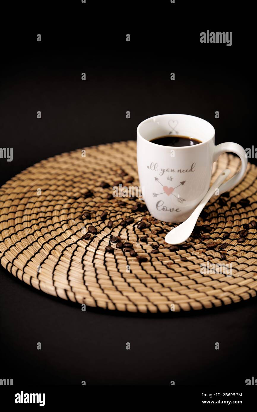 Taza de cerámica blanca con las palabras "todo lo que necesitas es amor" llena de café negro sobre una mesa de madera, y granos de café Foto de stock