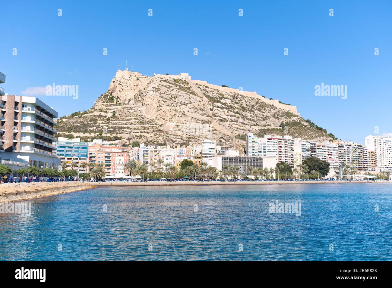Vista del Castillo de Santa Bárbara situado en el Monte Benacantil desde la playa en la costa de Alicante en el mar Mediterráneo en un día soleado azul brillante. Foto de stock