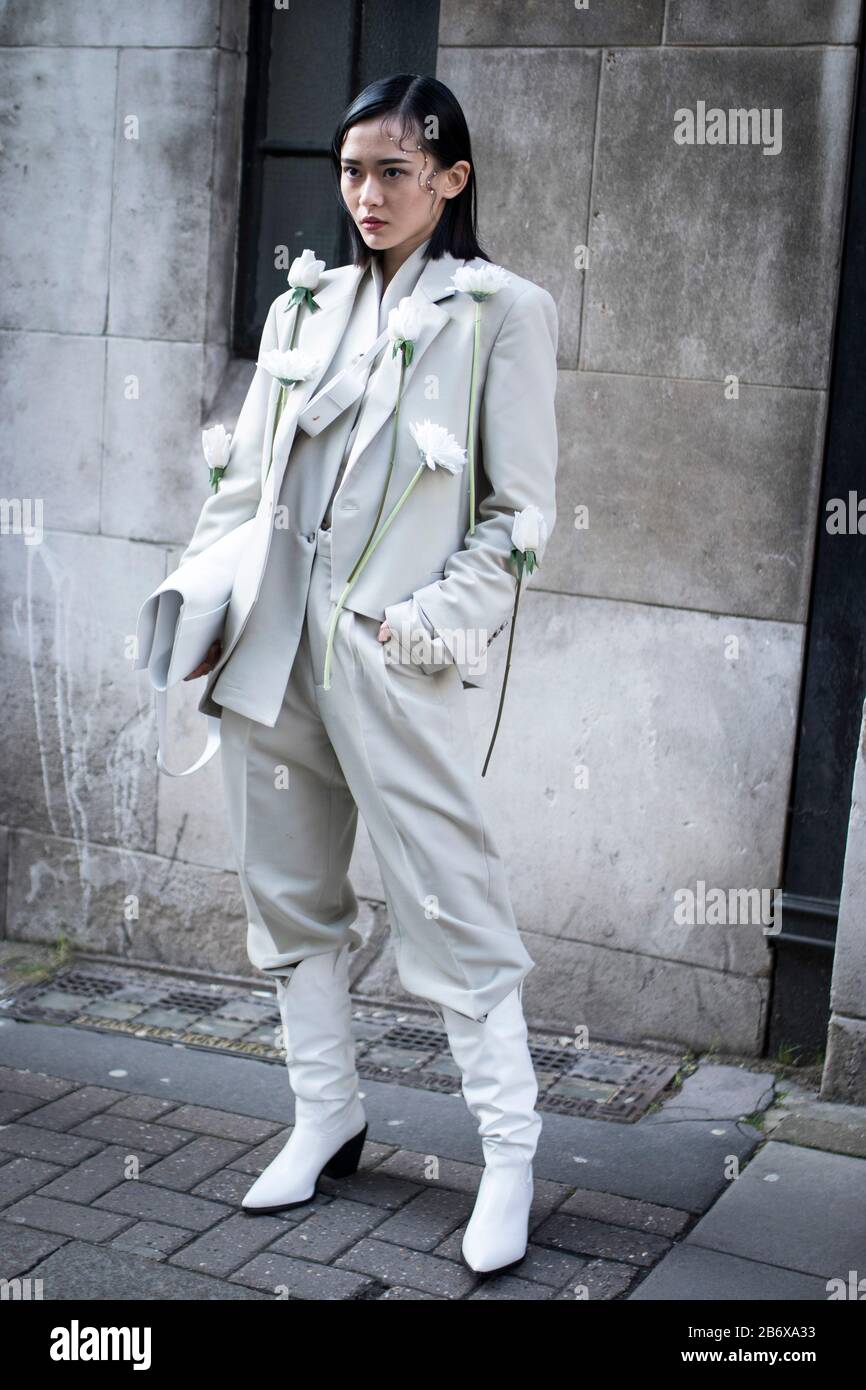 Londres, Reino Unido- febryary 15 2020: Gente de moda en la calle . Estilo  urbano. Una mujer en un abrigo largo blanco, pantsuit y botas. Gerberas y  rosas ar Fotografía de stock - Alamy