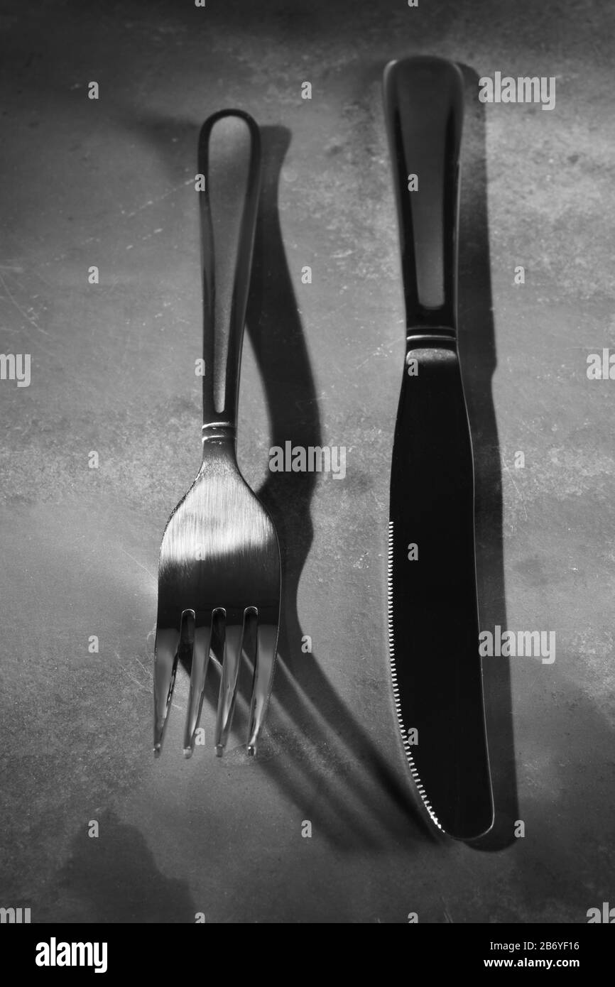Cuchillo y fork abstracto sobre pizarra natural en blanco y negro Foto de stock