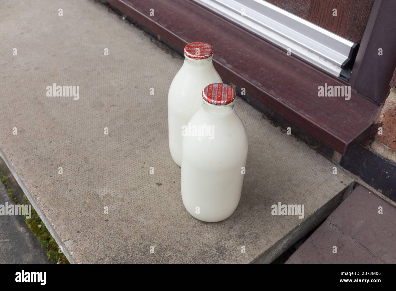 Leche fresca en botellas reciclables de pinta de vidrio entregadas a la puerta por un lechero tradicional Foto de stock