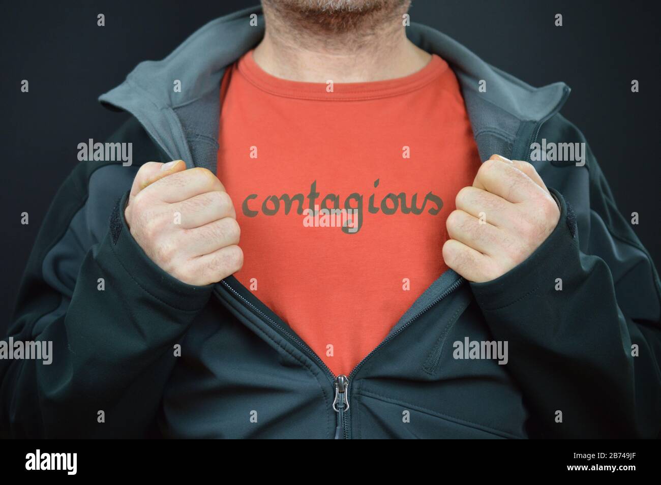 un hombre revelando un mensaje en su camiseta con la palabra contagiosa en ella bajo una chaqueta abierta Foto de stock