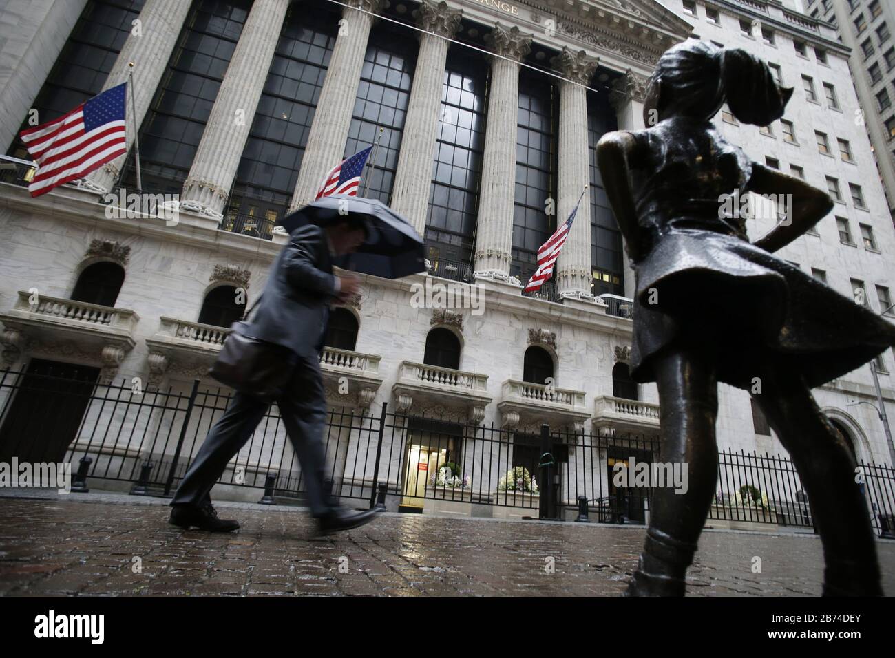 Nueva York, Estados Unidos. 13 de marzo de 2020. Un peatón sostiene un paraguas mientras camina por la Bolsa de valores de Nueva York en Wall Street en la ciudad de Nueva York el viernes, 13 de marzo de 2020. Las acciones cedieron la mayor parte de un repunte inicial el viernes, intentando recuperarse de las fuertes pérdidas de la sesión anterior, con el Dow Jones Industrial Average por debajo de 2000 puntos y 10 por ciento, que fue el peor desde la caída del mercado del "lunes negro" en 1987. Foto de John Angelillo/UPI crédito: UPI/Alamy Live News Foto de stock