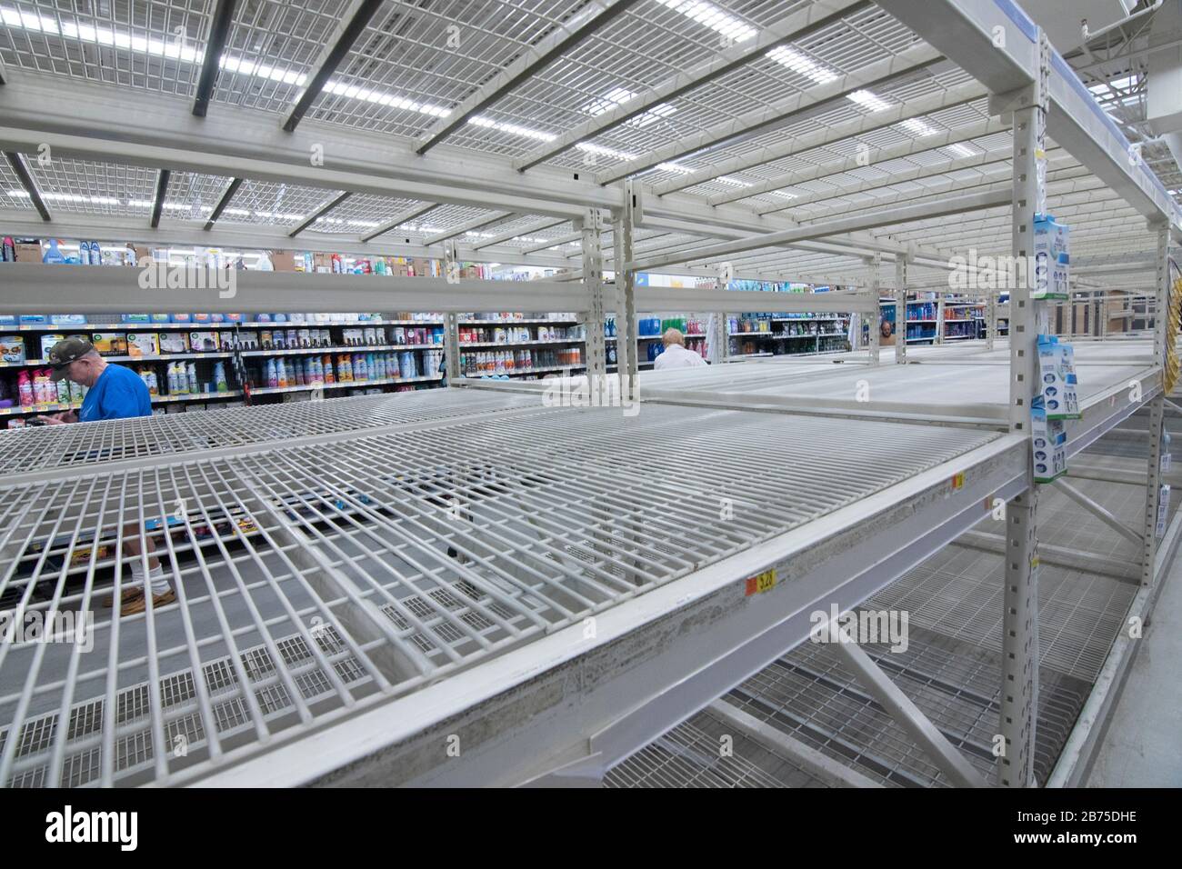 Los compradores no identificados van por estantes vacíos en la tienda Walmart en Englewood, Florida USA 3/13/2020. Normalmente estos estantes estarían llenos de papel pro Foto de stock