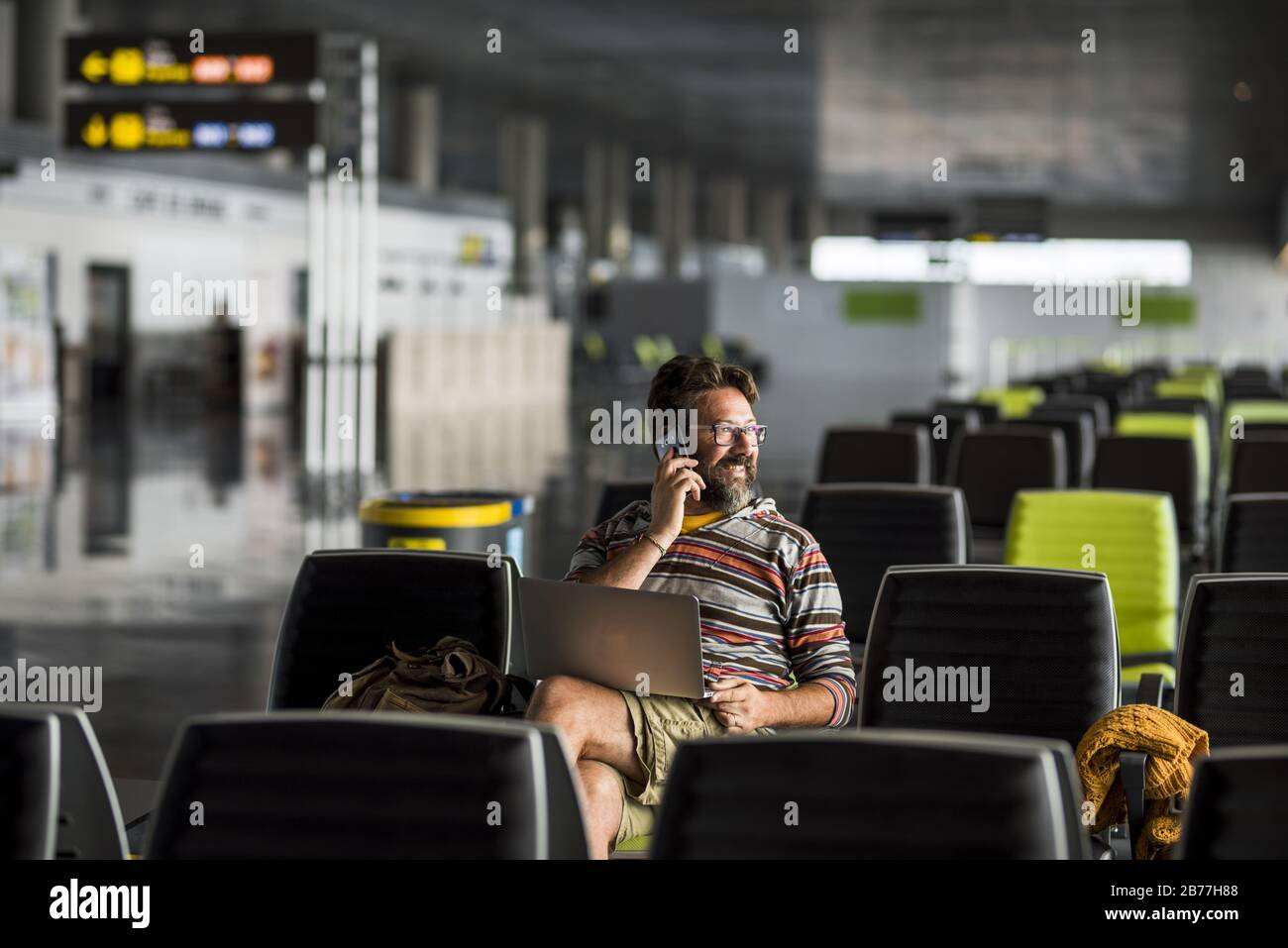 Hombre adulto que viaja en el aeropuerto se sienta en la puerta esperando su vuelo del plan de vuelo - el conncept del retraso y la gente que trabaja por todas partes con el ordenador portátil Foto de stock