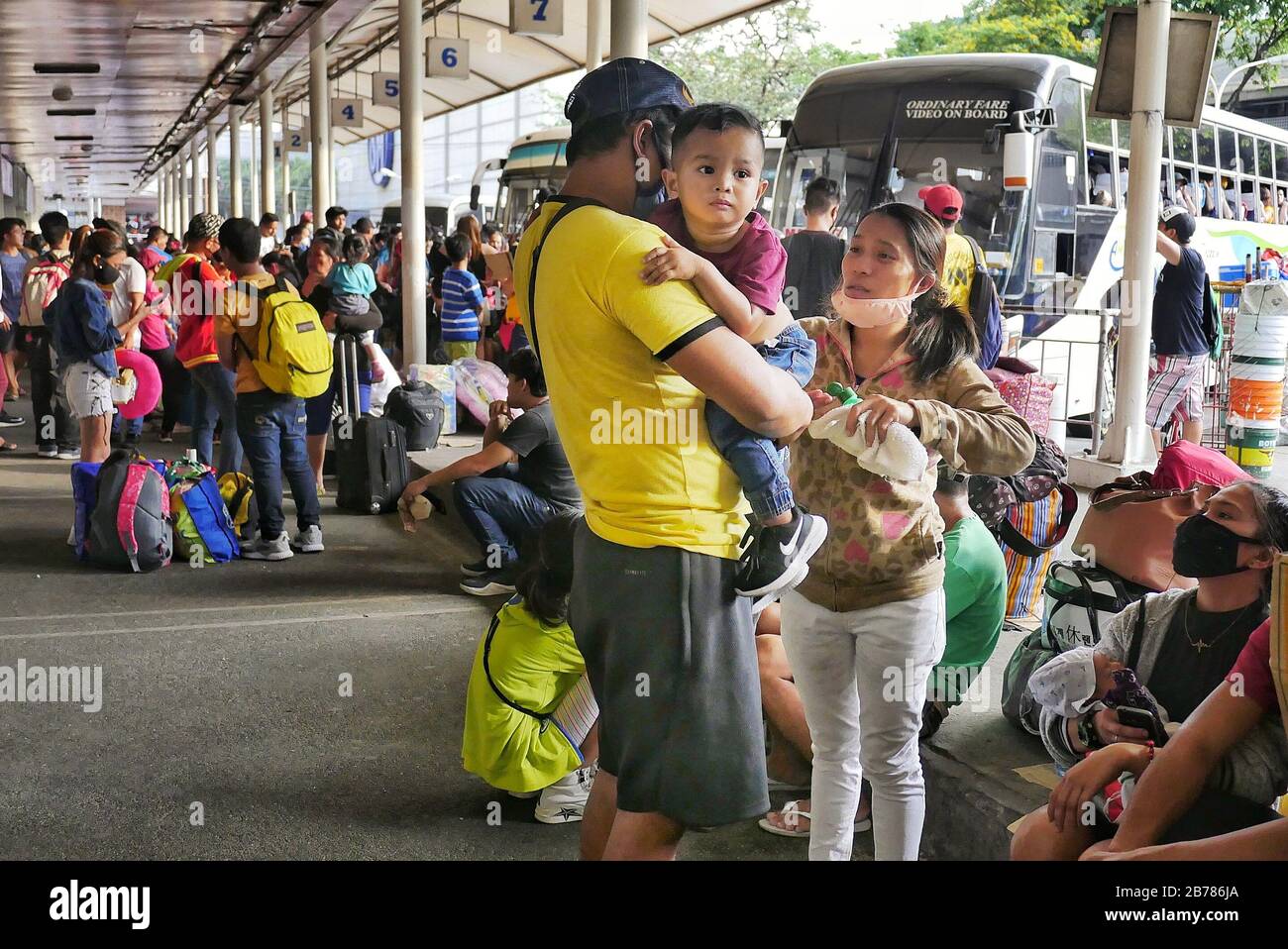 Ciudad De Quezon, Región Capital Nacional, Filipinas. 14 de marzo de 2020. Una madre aplicando alcohol de frotamiento sobre su hijo mientras esperan su viaje en autobús. Crédito: George Buid/Zuma Wire/Alamy Live News Foto de stock