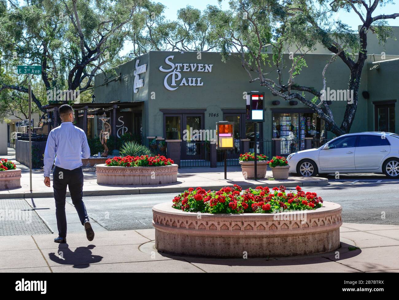 Un hombre se acerca a un cruce de peatones junto a plantadores de begonias rojas frente al edificio Steven Paul Hair Salon en el hermoso Old Town Scottsdale, AZ Foto de stock