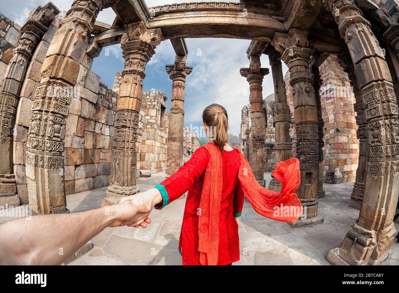 Mujer en traje rojo con bufanda que lleva al hombre a mano a la torre de Qutub Minar en Delhi, India Foto de stock