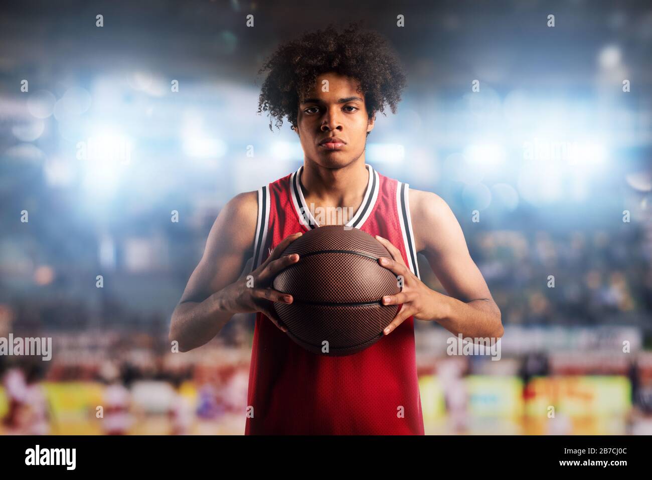 El jugador de baloncesto sostiene la pelota en la canasta en el estadio lleno de espectadores. Foto de stock