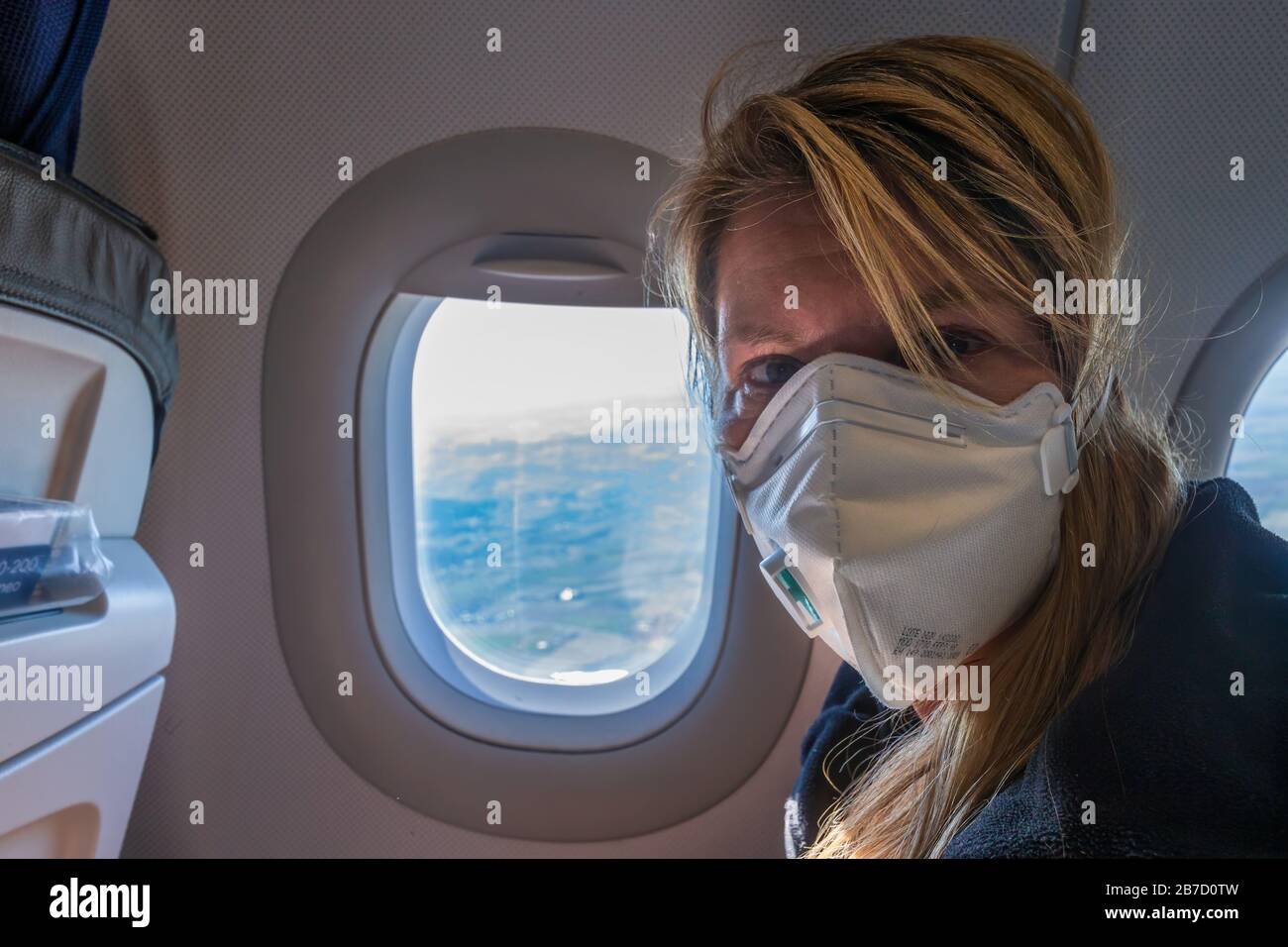 Europa - 15 de marzo de 2020: Mujer en un avión con máscara facial para la protección contra el virus sars-cov-2 Foto de stock